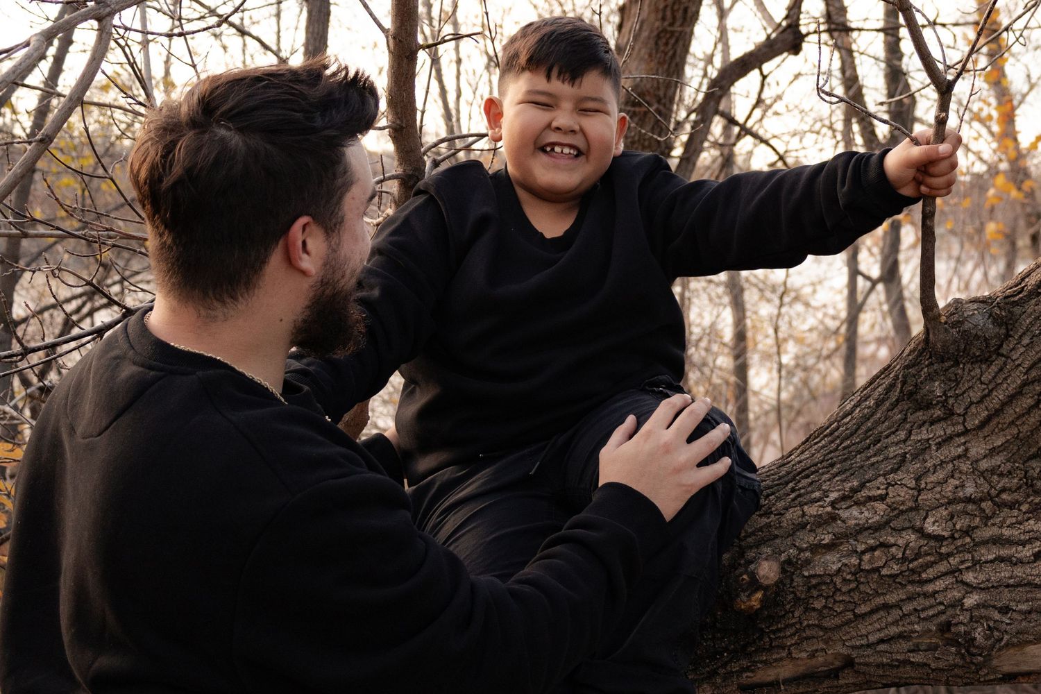 A man helps a laughing boy climb a tree in an autumn forest in Winnipeg