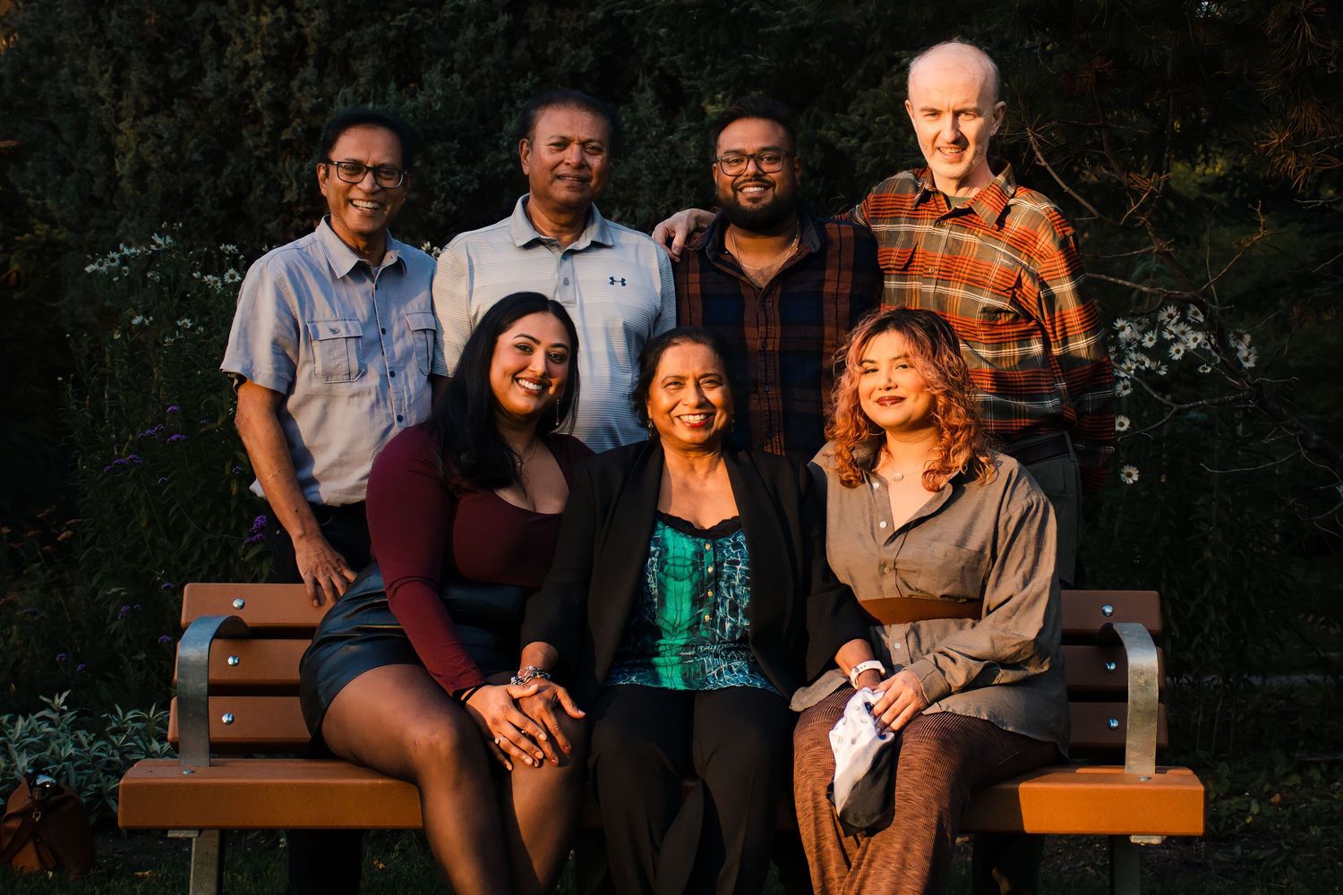 Family group portrait of seven people sitting and standing on benches in a garden at golden hour in Winnipeg