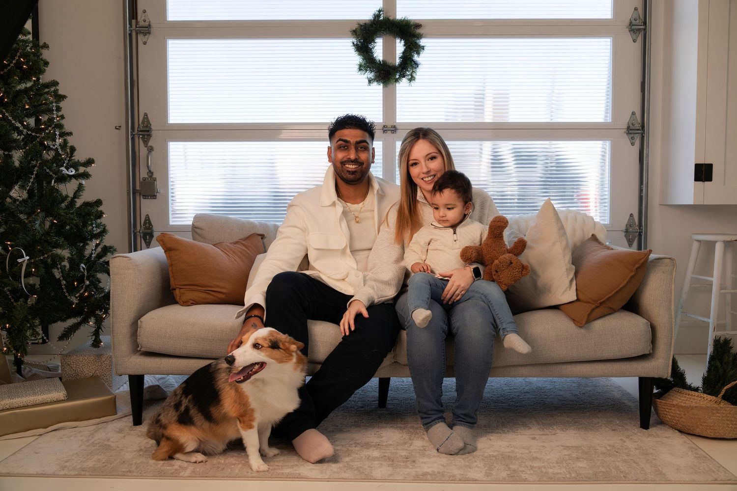 Happy family with a Corgi dog posing on a sofa with Christmas wreath decor.
