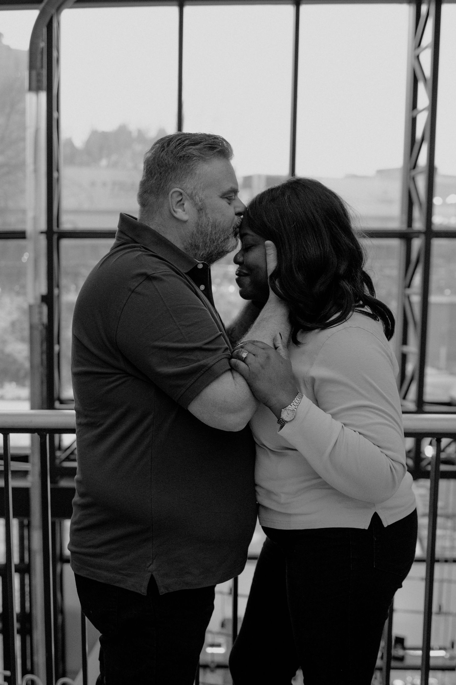 Black and white photo of a couple sharing an intimate moment, embracing and touching foreheads indoors.