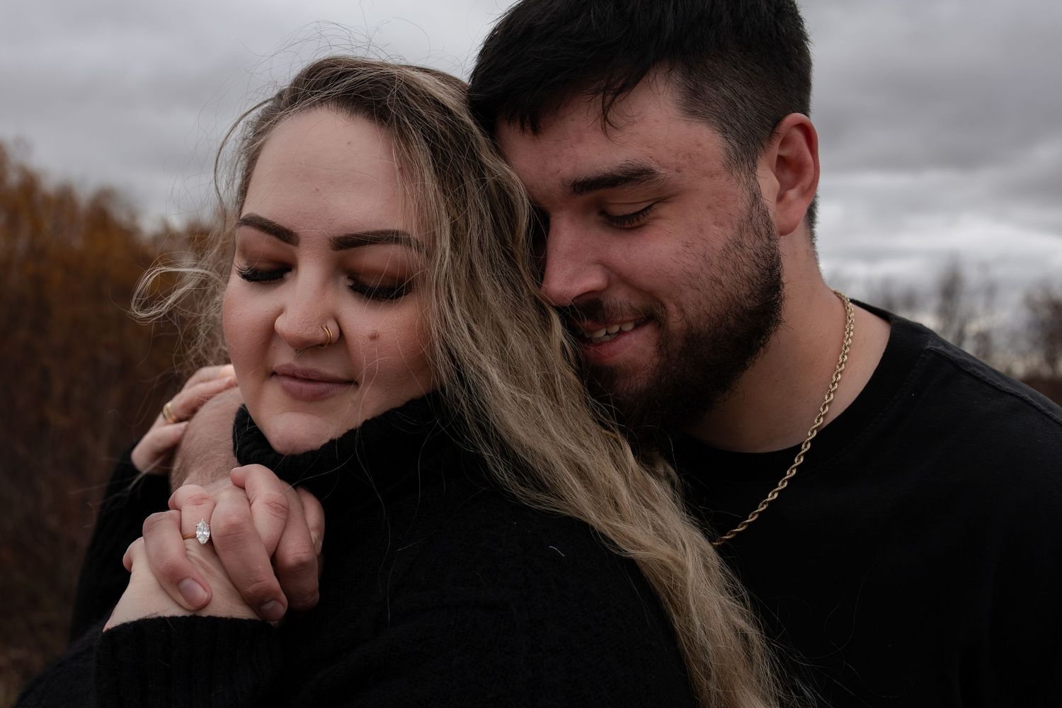 Couple in black outfits share tender moment holding hands during autumn engagement photo session in Winnipeg