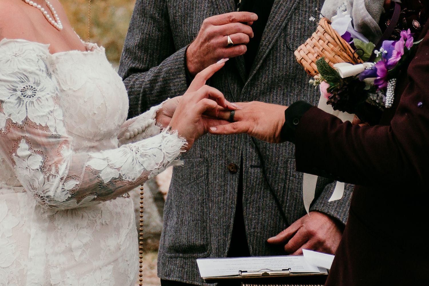 Close-up of wedding ring exchange ceremony with bride in lace gown and groom in grey suit in Winnipeg