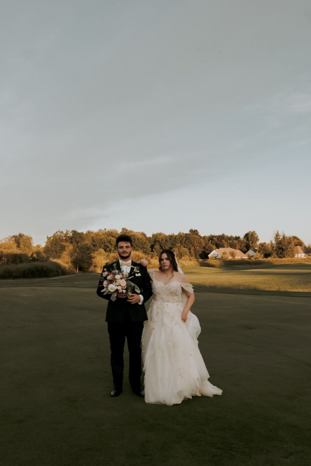 Wedding couple walks together across an open field at golden hour.