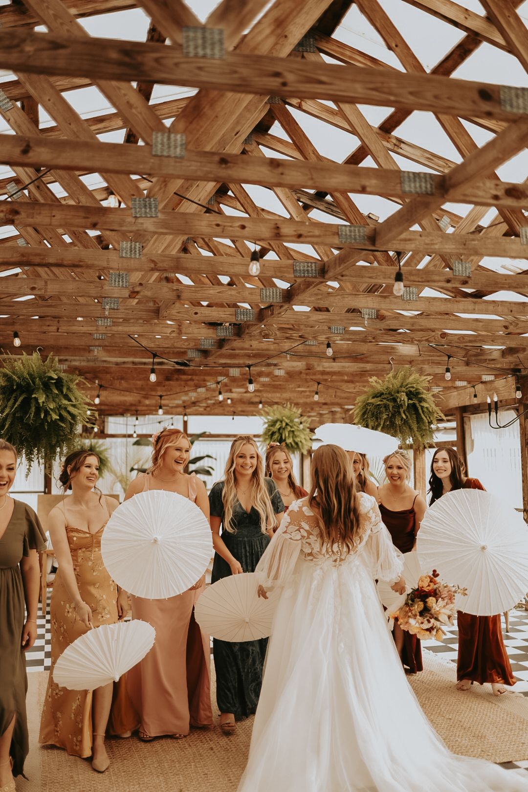 Wedding scene with white parasols under rustic wooden ceiling and hanging greenery.