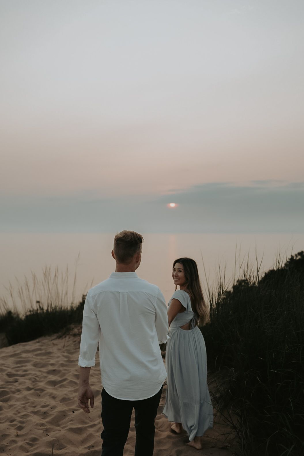 Two people walk hand in hand along sandy dunes at sunset.