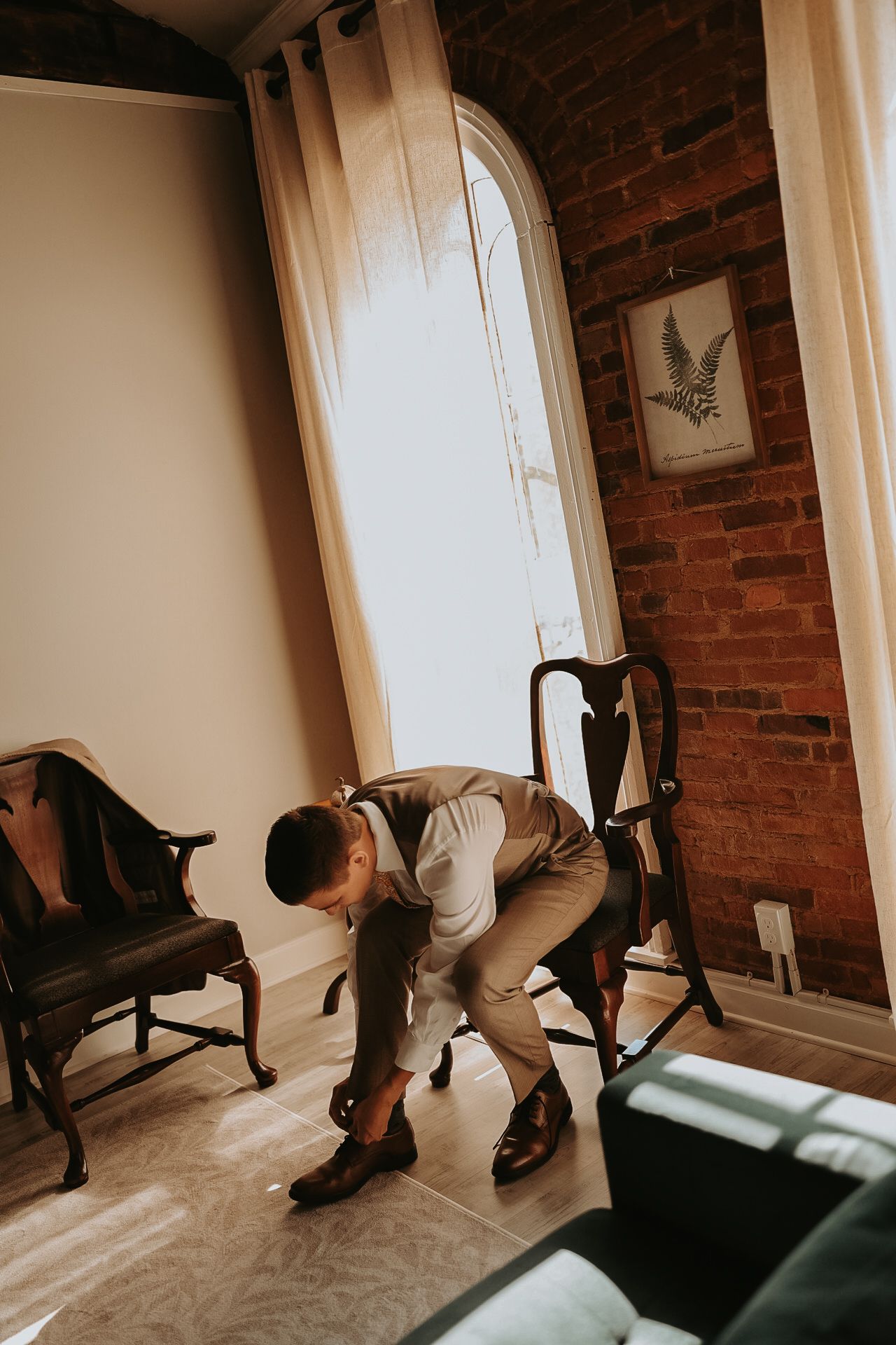 Person putting on dress shoes while sitting in a vintage chair against exposed brick walls.