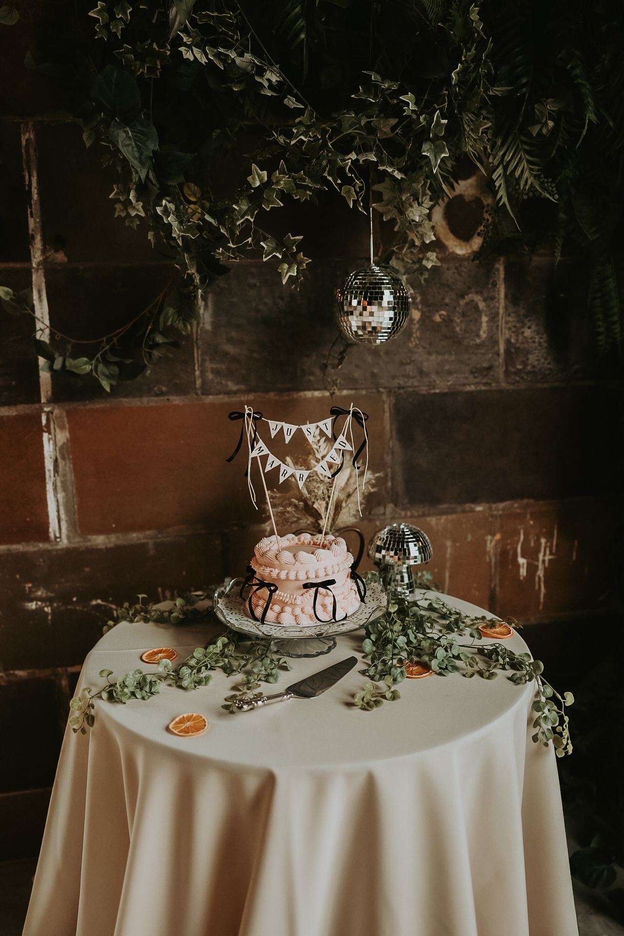 Elegant wedding cake display on white tablecloth with greenery accents.