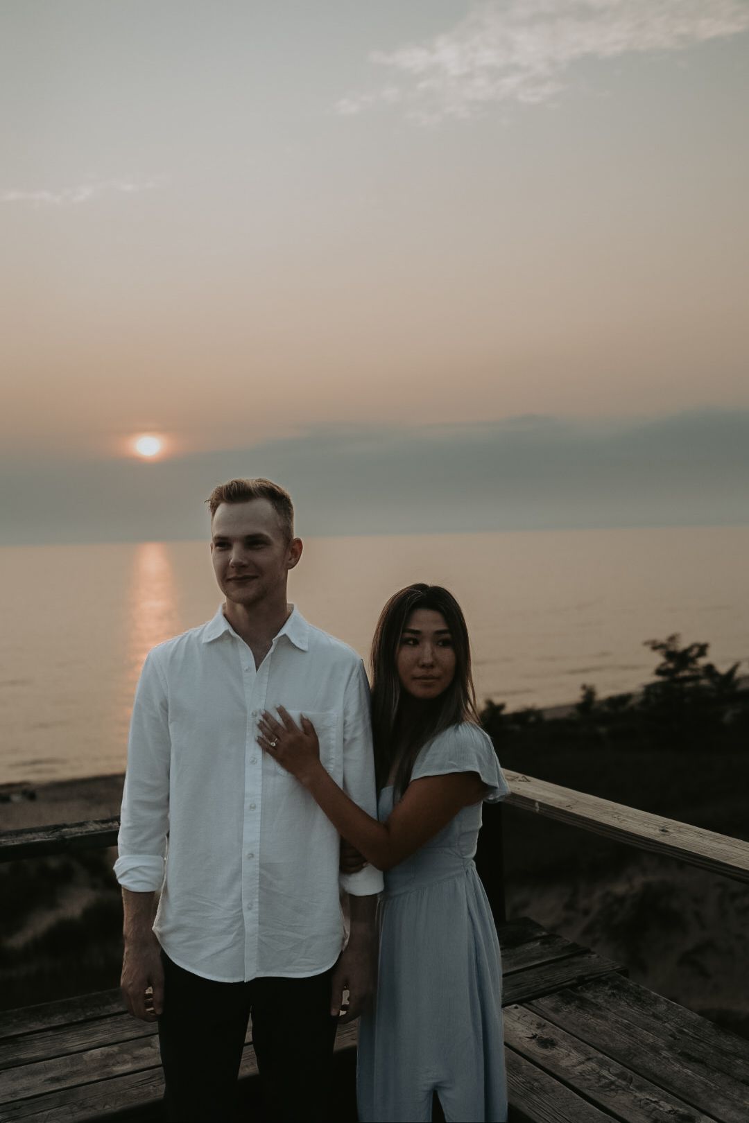 A couple shares a tender moment against a sunset ocean backdrop.