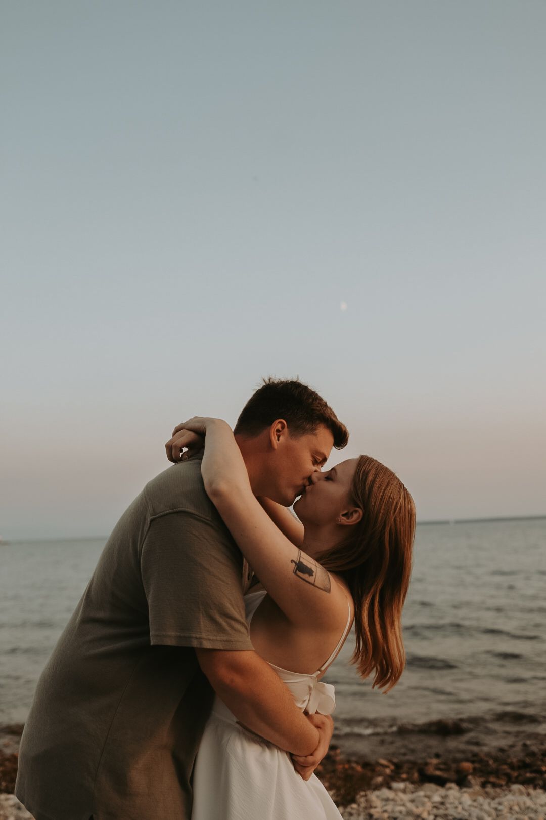 A tender moment captured between a couple on a rocky beach at sunset.