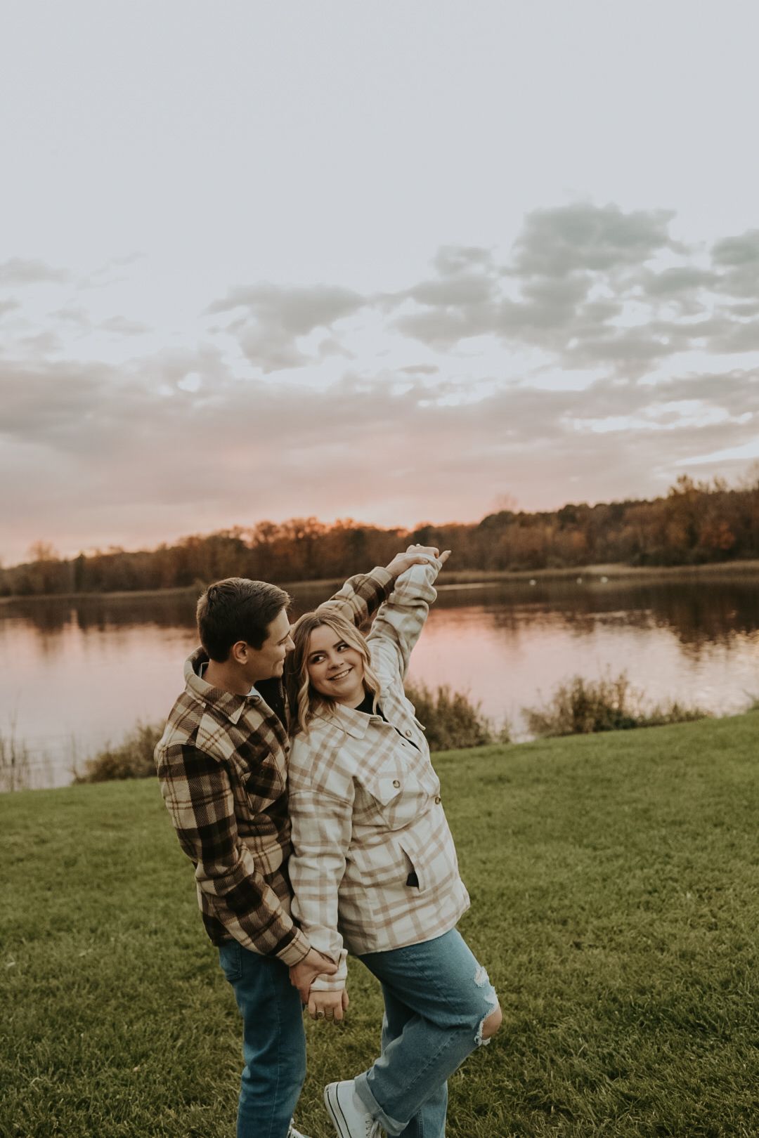 Two people in plaid shirts dance together by a lake at sunset.