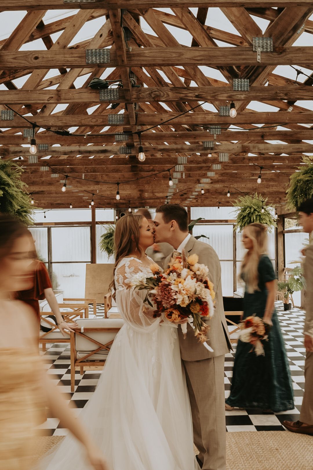 Wedding couple shares an intimate moment under rustic wooden beams with autumn-colored floral arrangements.