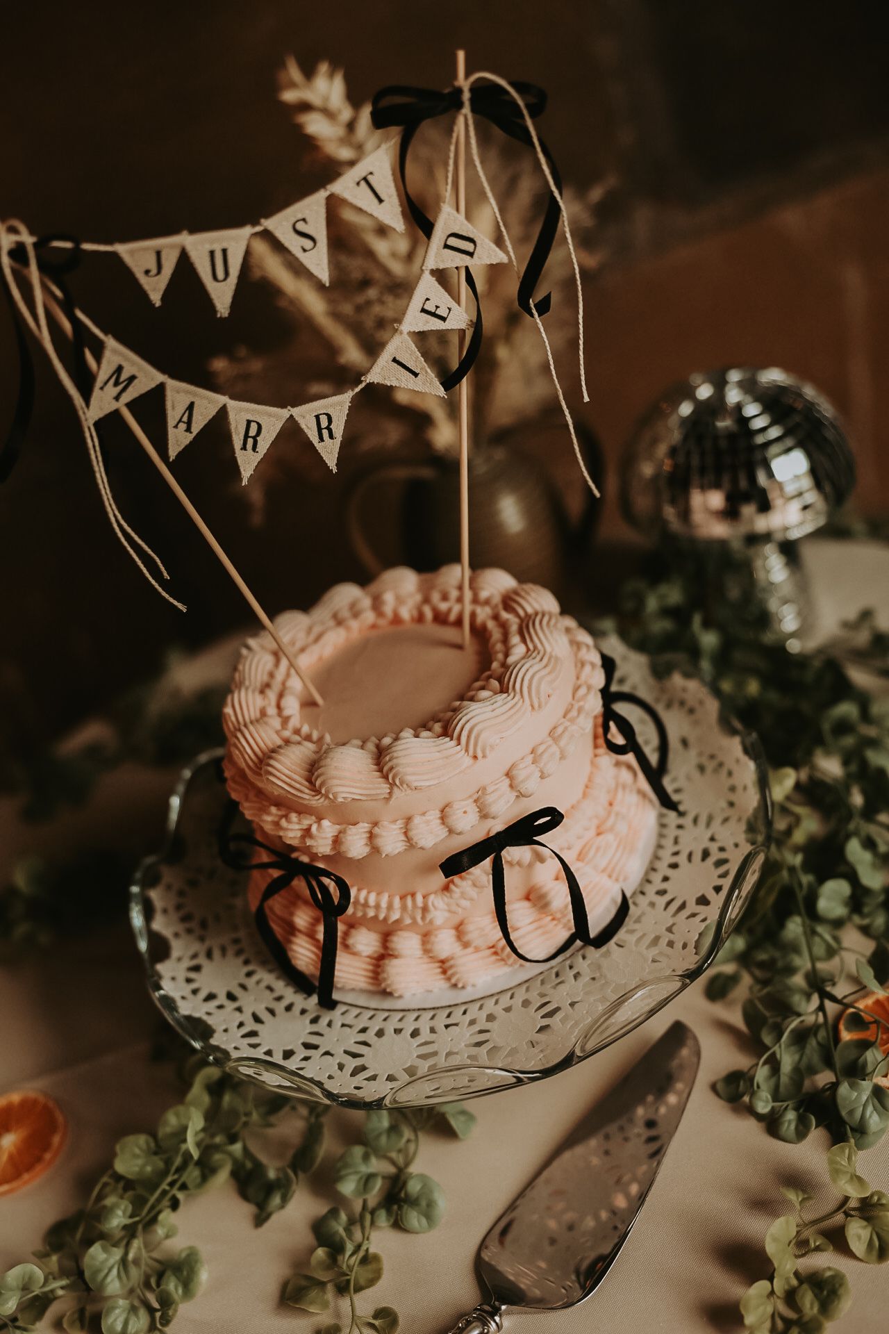 Vintage-style wedding cake decorated with pink frosting and bunting on lace doily.