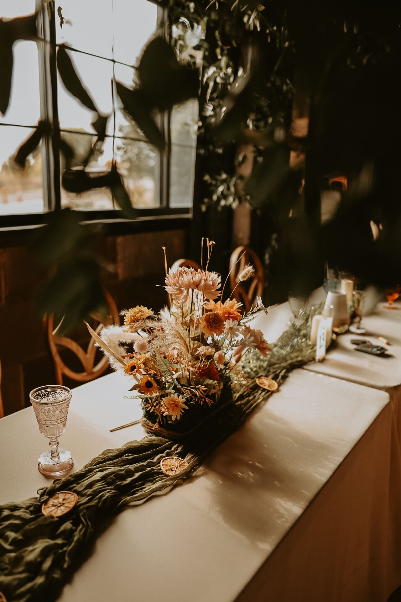 Moody wedding table setting with dried flower centerpiece and vintage glassware in warm lighting.
