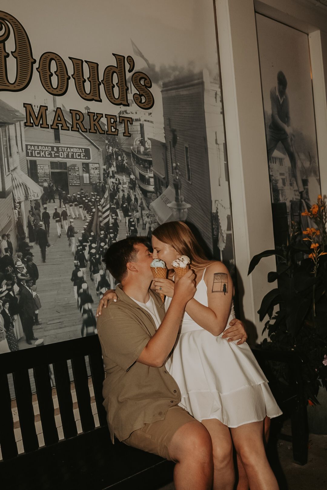 A couple shares an intimate moment while sitting on a bench in front of a vintage storefront.