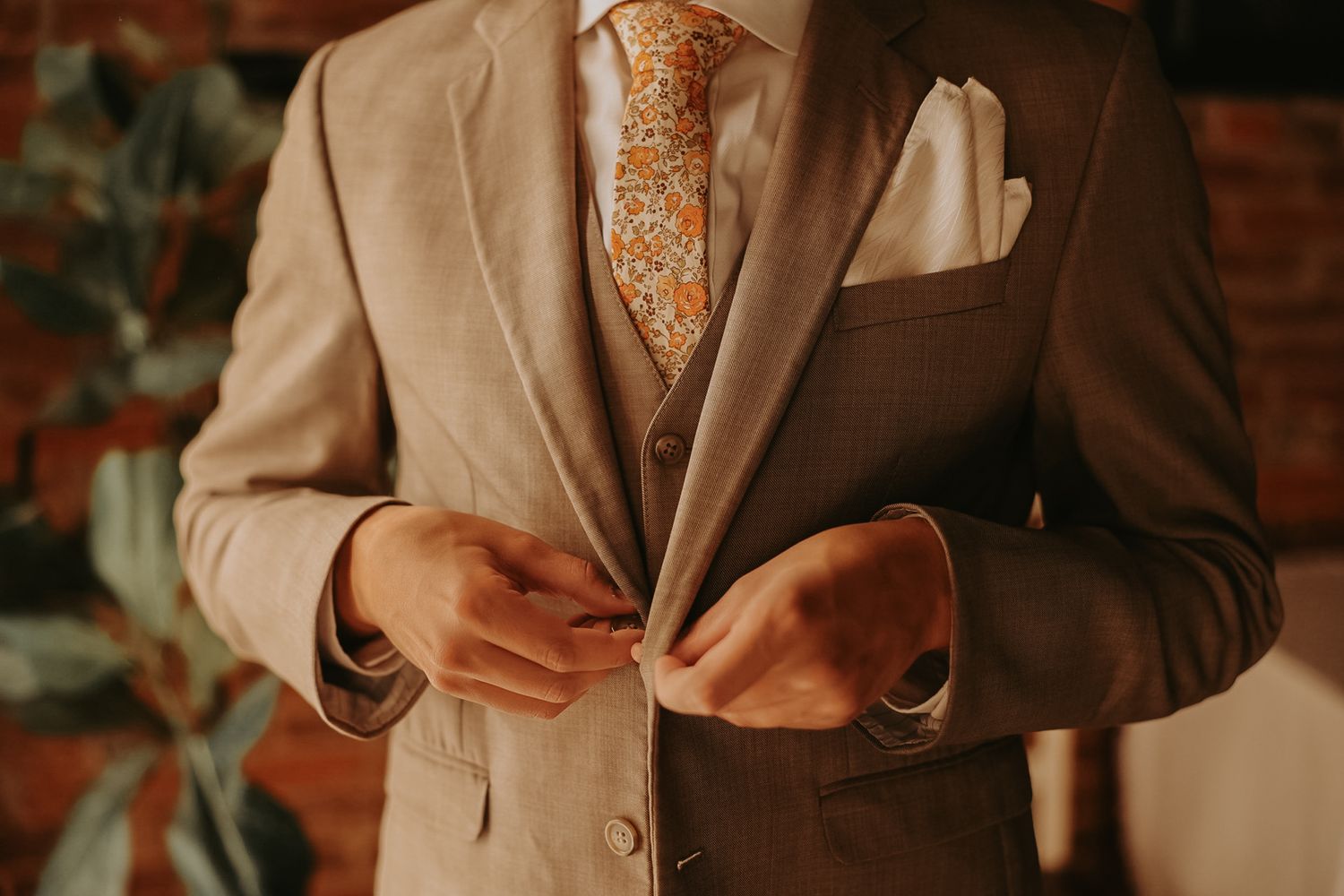 Detail shot of a tan suit jacket and orange patterned tie being adjusted.