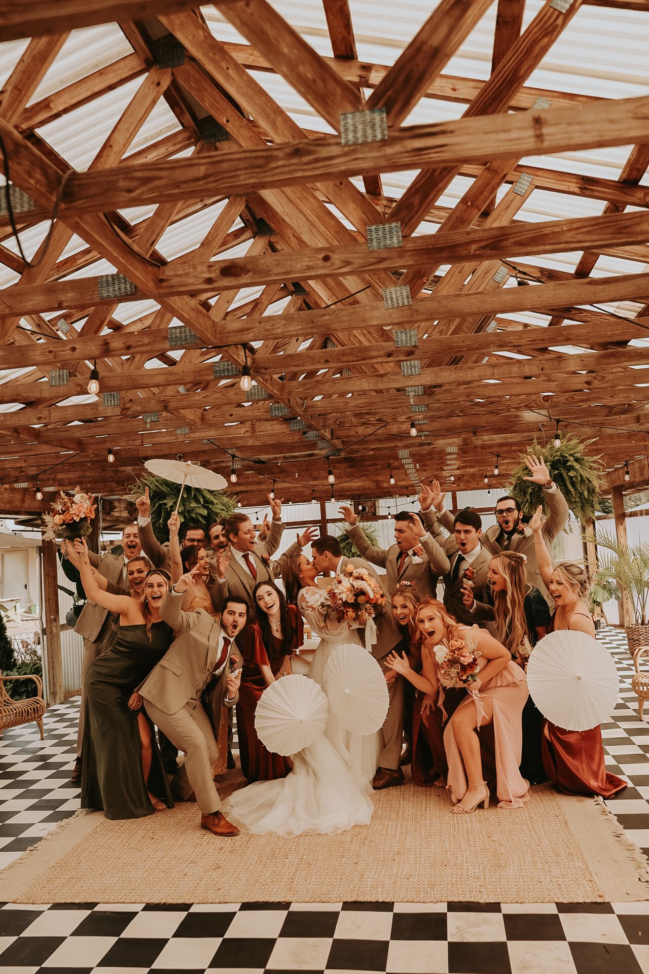 Wedding celebration group photo under rustic wooden beams with checkered flooring.