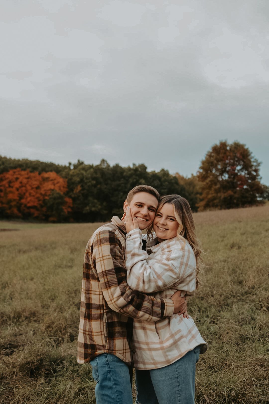 Embrace in autumn field with fall colors and cloudy sky.