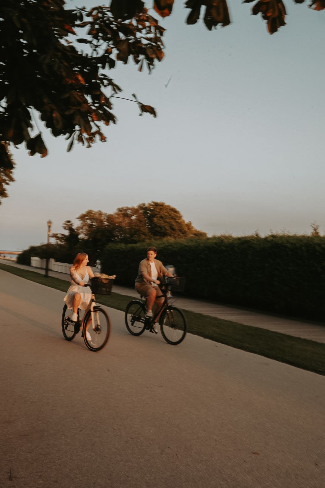 Two people ride bicycles together along a scenic path at sunset.