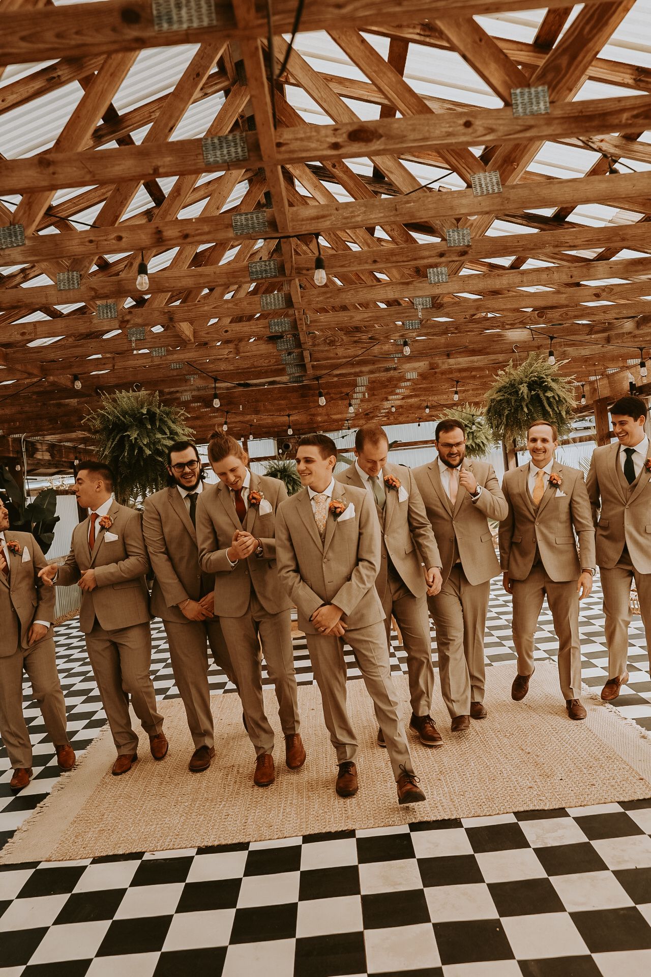 Wedding party in matching tan suits lined up under rustic wooden rafters.
