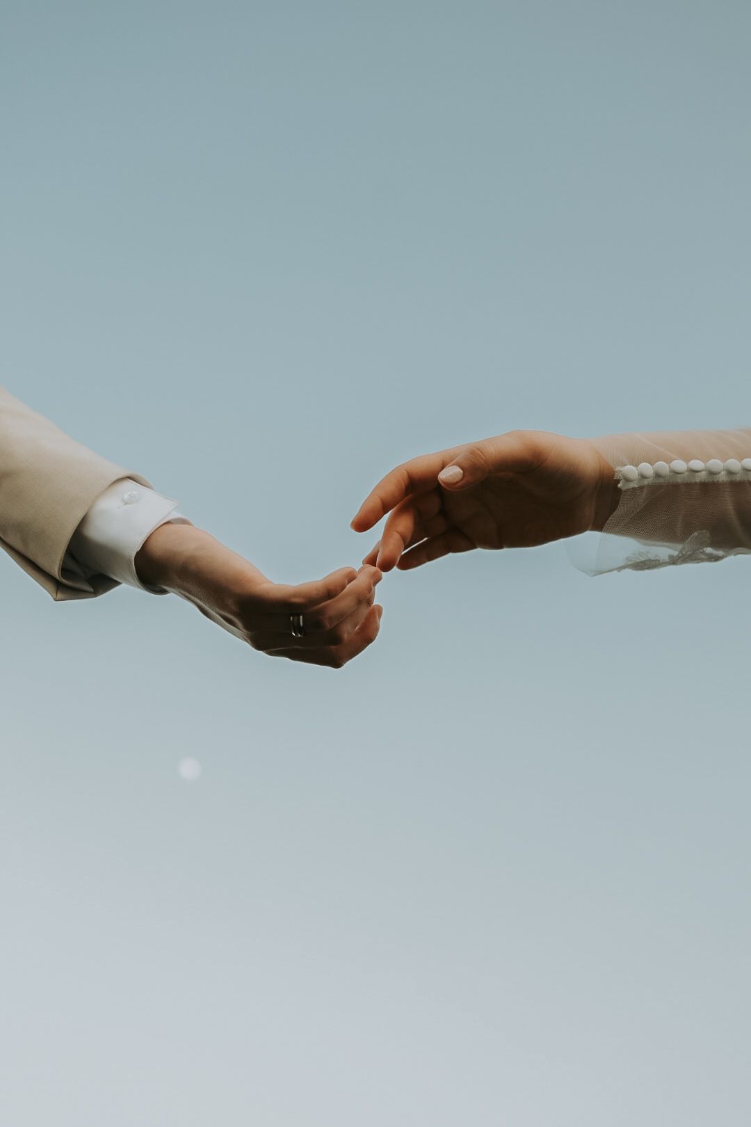 Artistic close-up of hands reaching toward each other against blue sky background.
