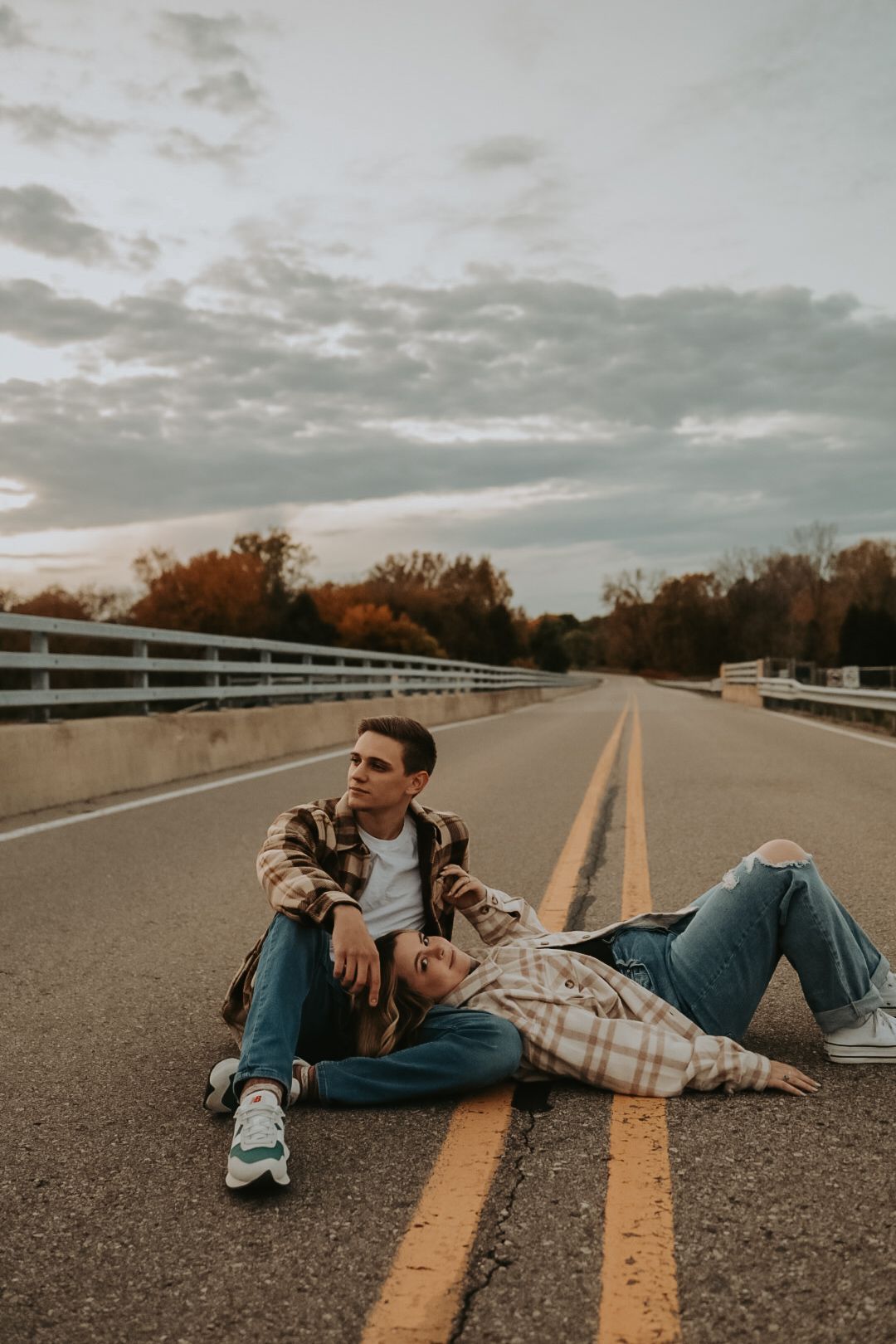 Two people relaxing on empty road with dramatic cloudy sky overhead.