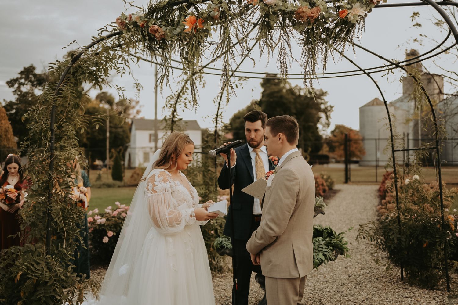 Romantic outdoor wedding scene with floral archway and fall colors in the background.
