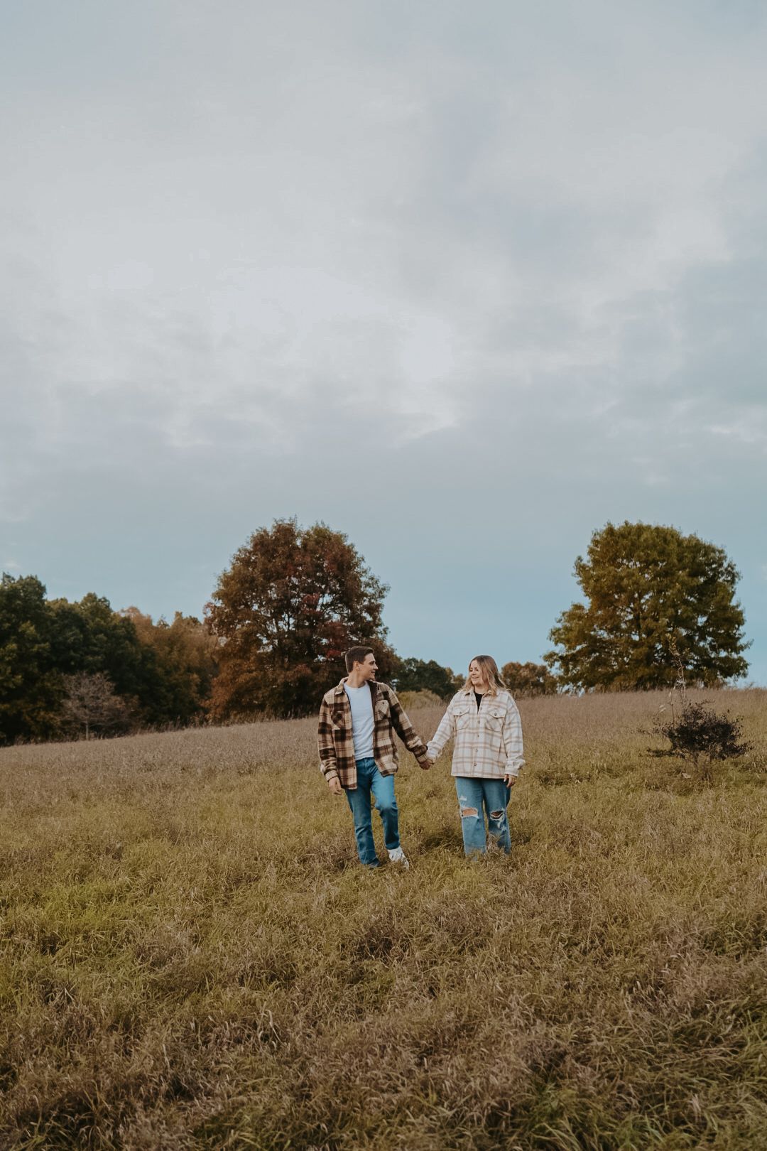 Two people walk hand in hand across a hilltop meadow during autumn.