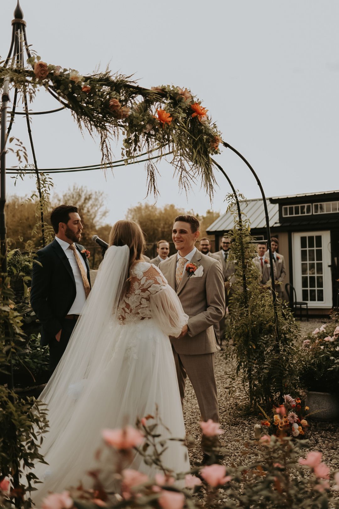 Intimate wedding ceremony in garden setting with floral-decorated metal archway.
