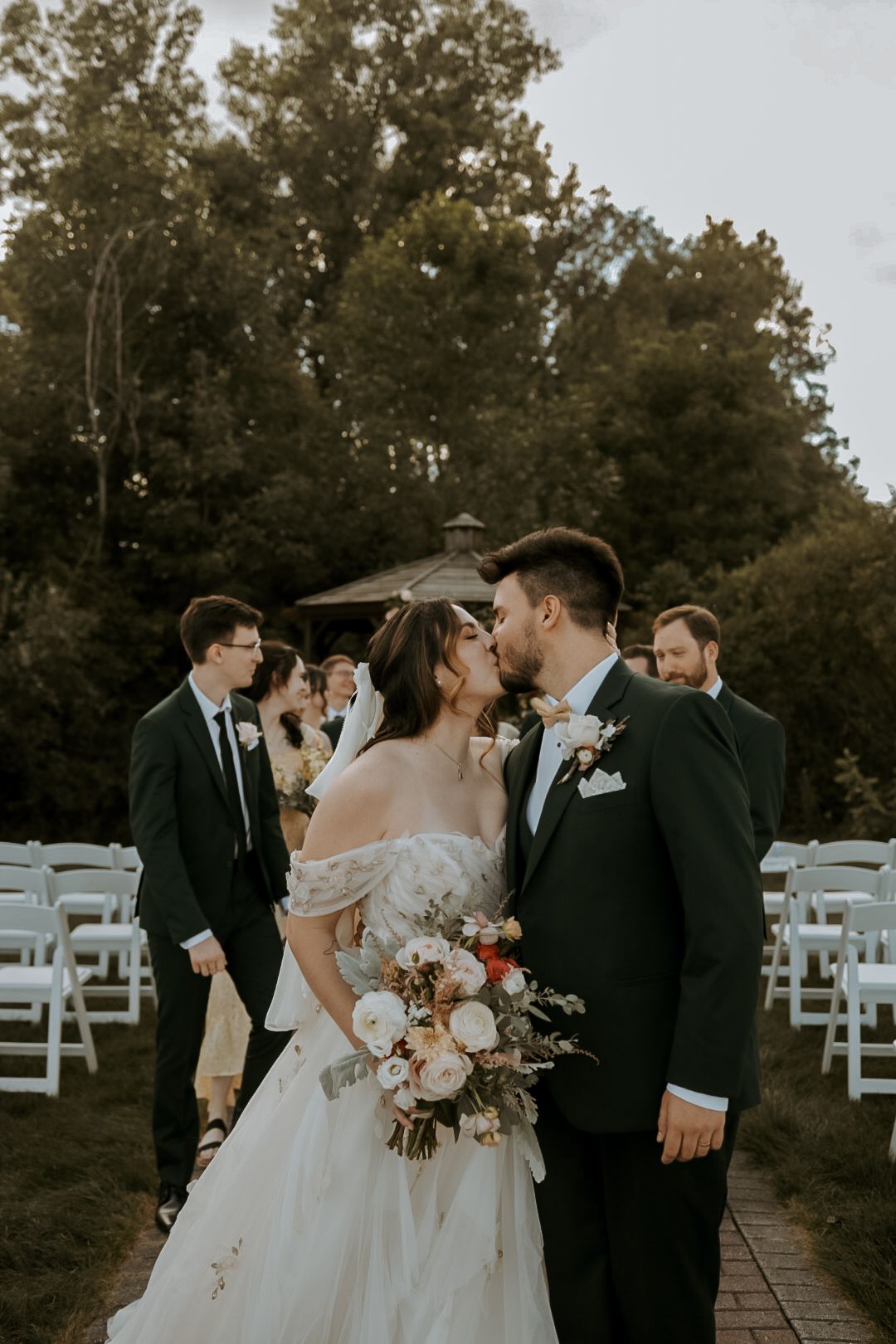 A romantic outdoor wedding ceremony scene with white chairs and autumn trees in the background.