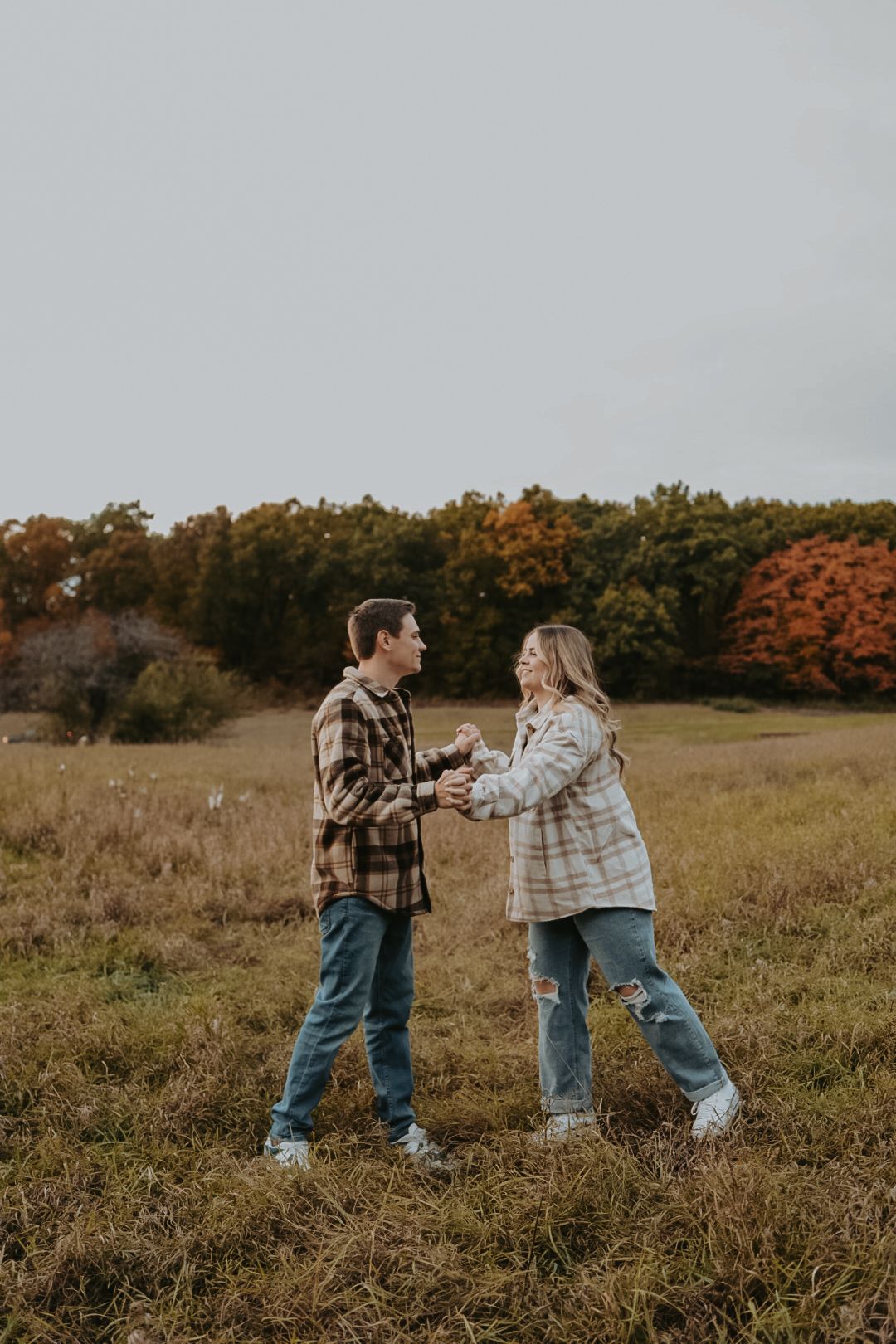 Couple in matching plaid shirts dancing in autumn field.