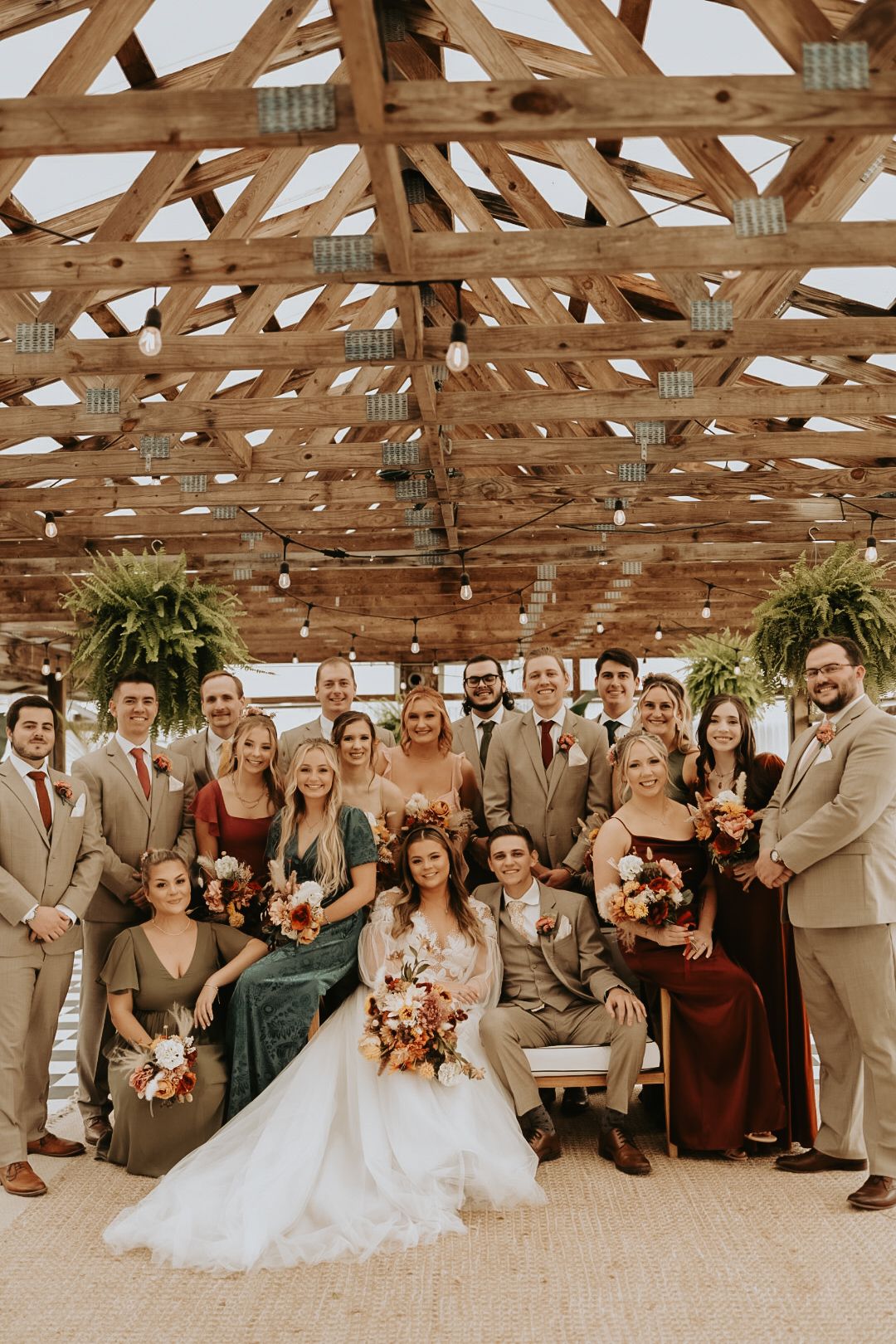 Wedding party poses for group photo in rustic venue with wooden beams and natural lighting.