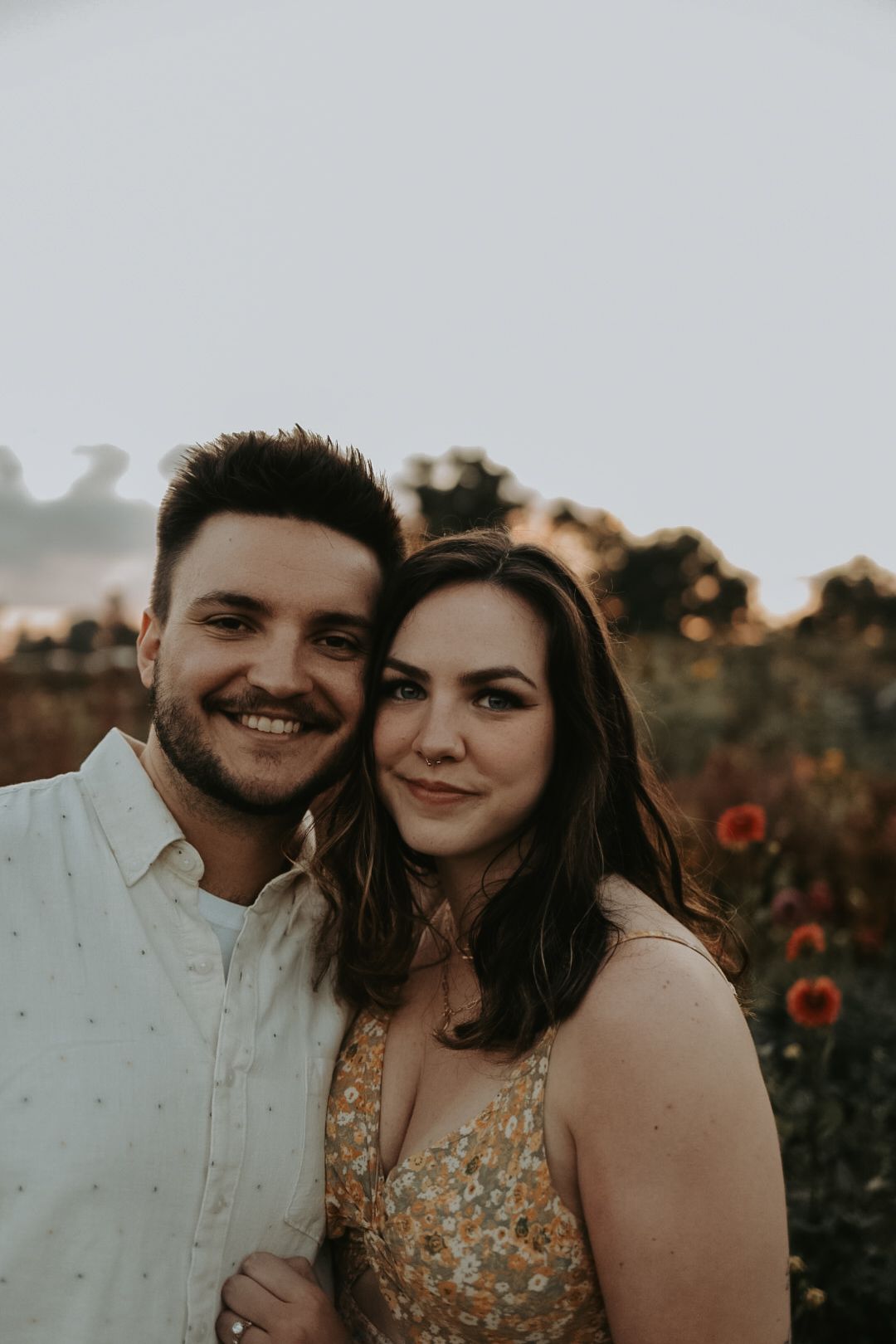 Couple poses together in a flower field at sunset.