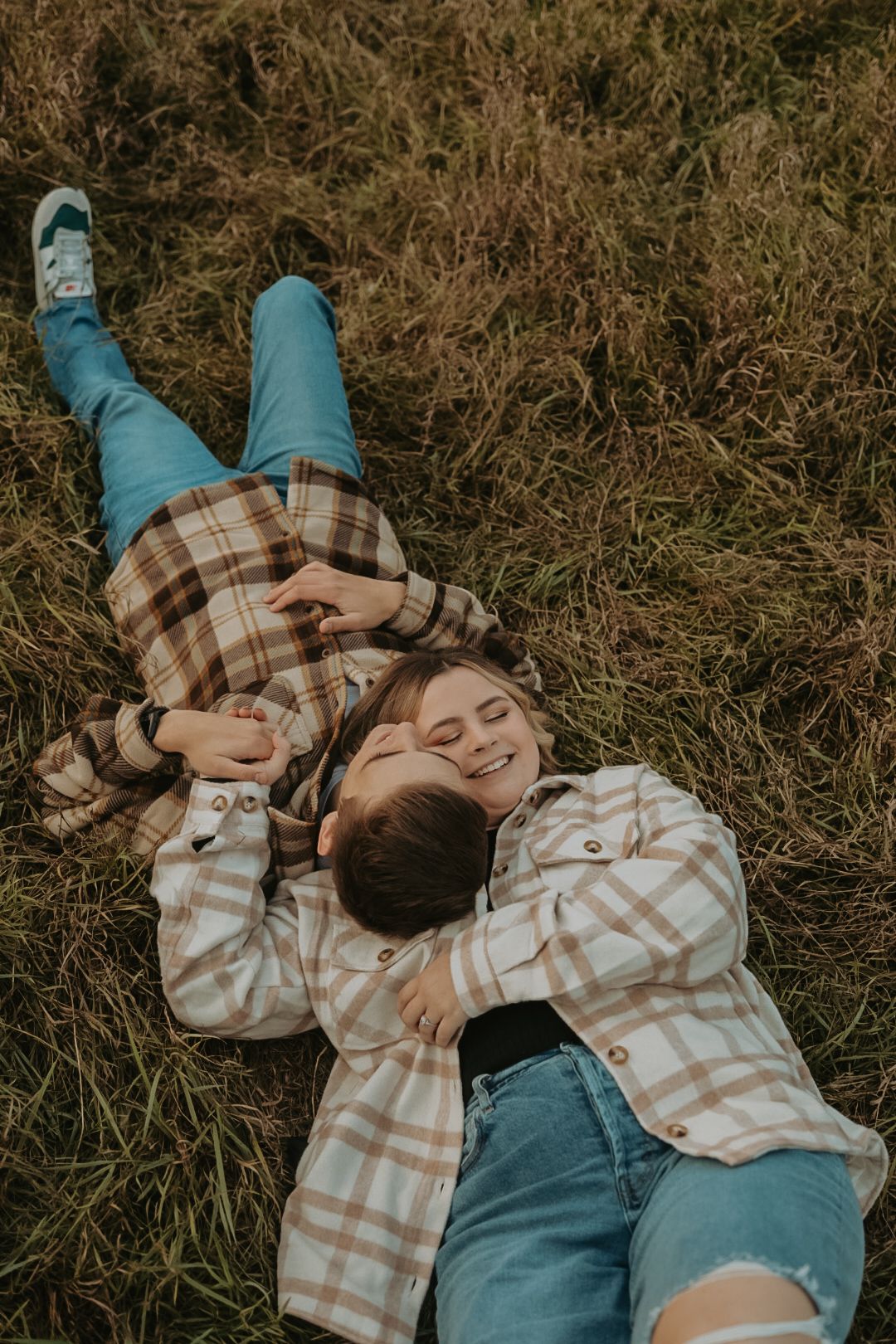 A couple relaxes together on dried grass wearing coordinated plaid outfits.
