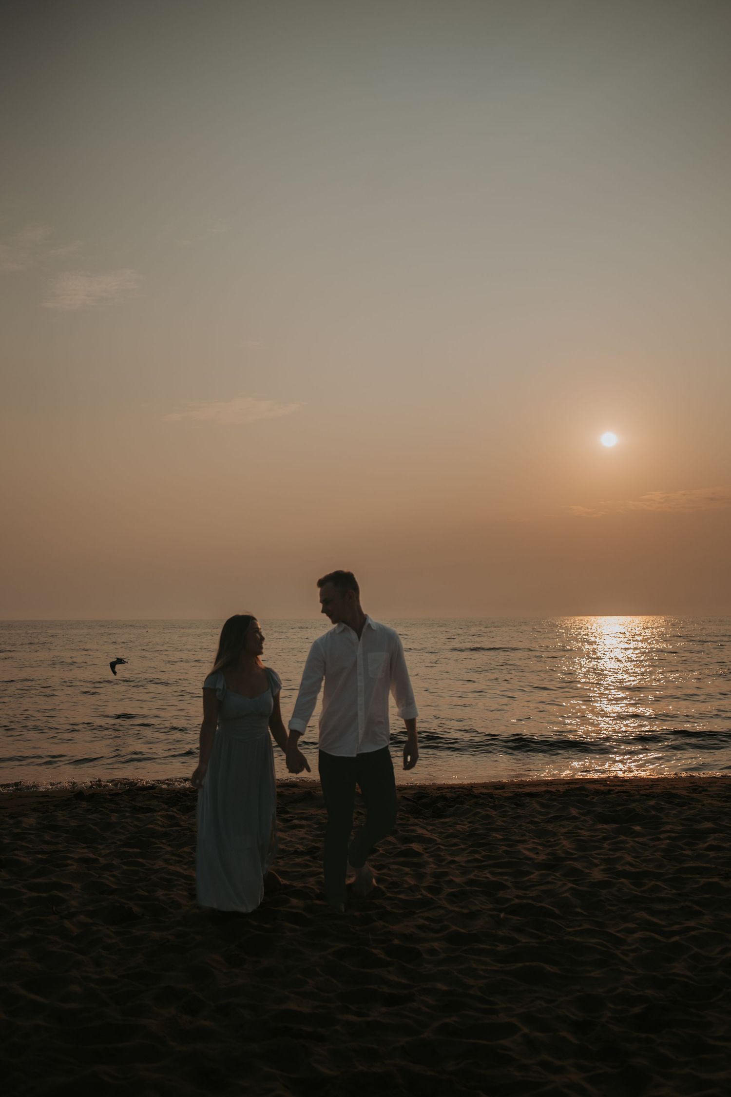 A romantic beach scene at sunset with two figures standing by the ocean.