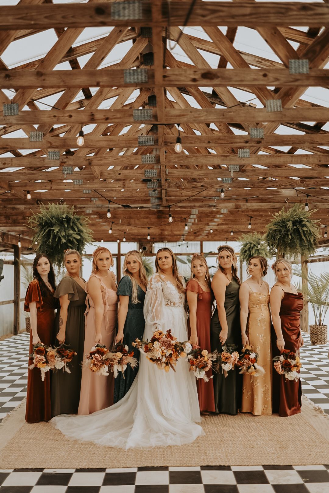 Bridal party in autumn-colored dresses posing under rustic wooden rafters.