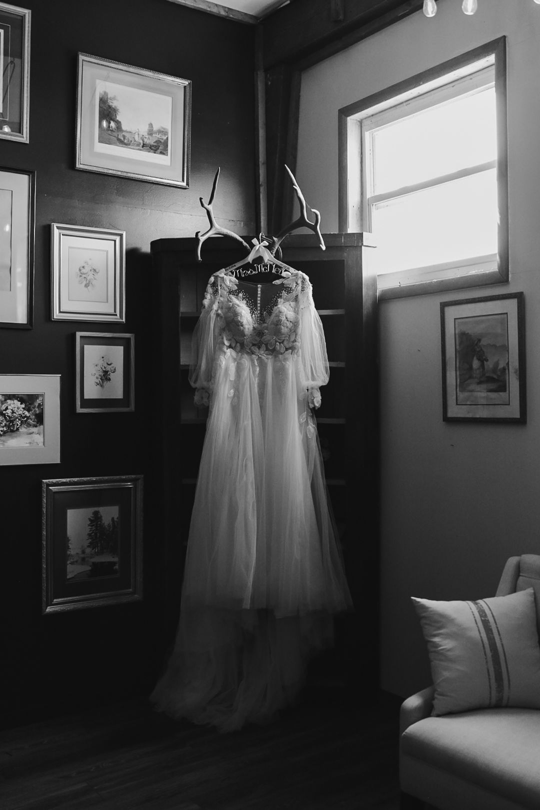 Black and white photo of an elegant wedding gown displayed in a room with gallery wall and natural lighting.
