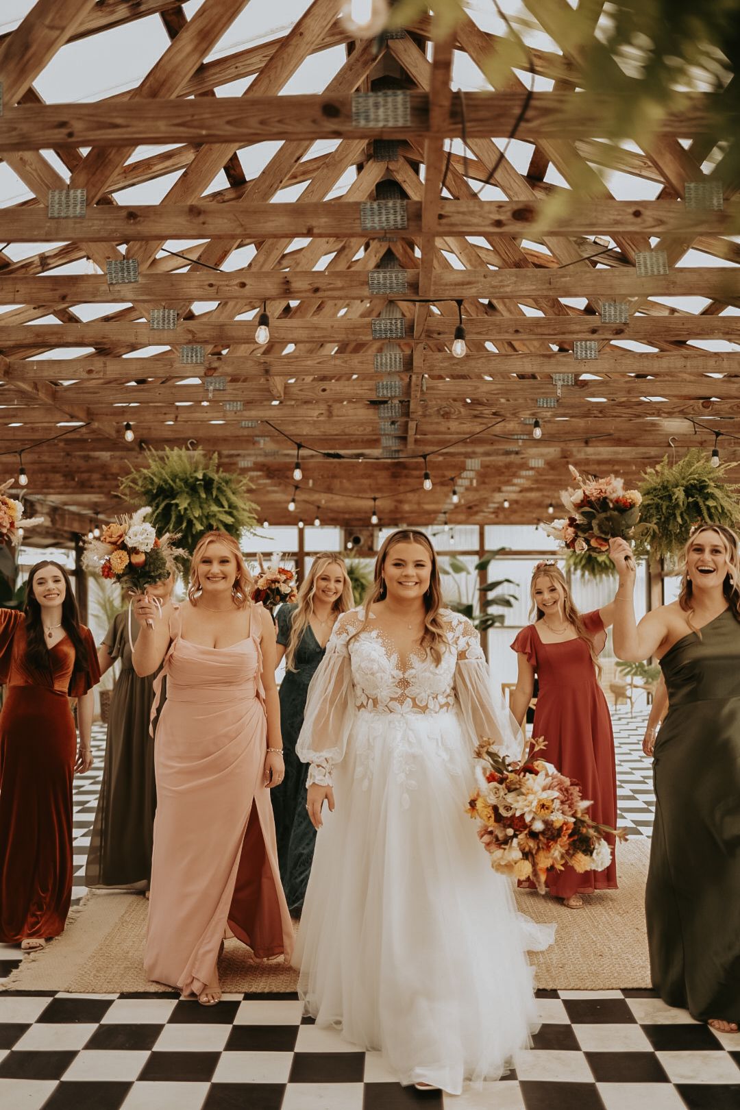 Wedding party walking on checkered floor under wooden beams with autumn floral bouquets.