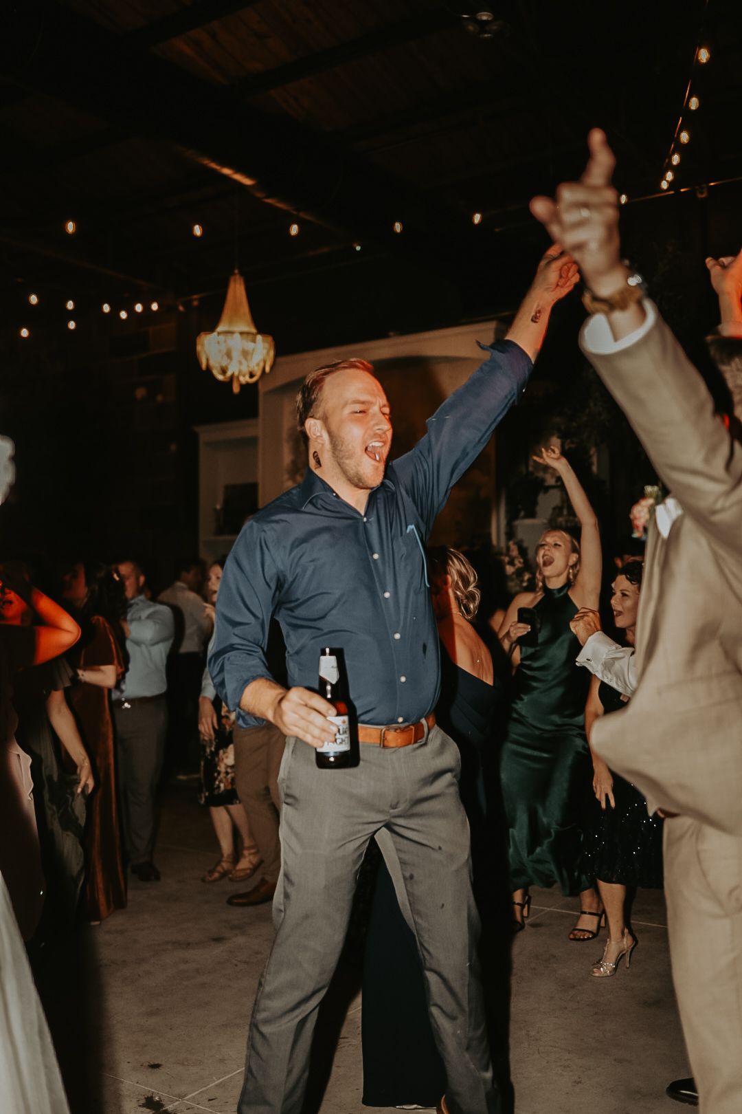 Wedding guests dancing and celebrating at a dimly lit reception venue.