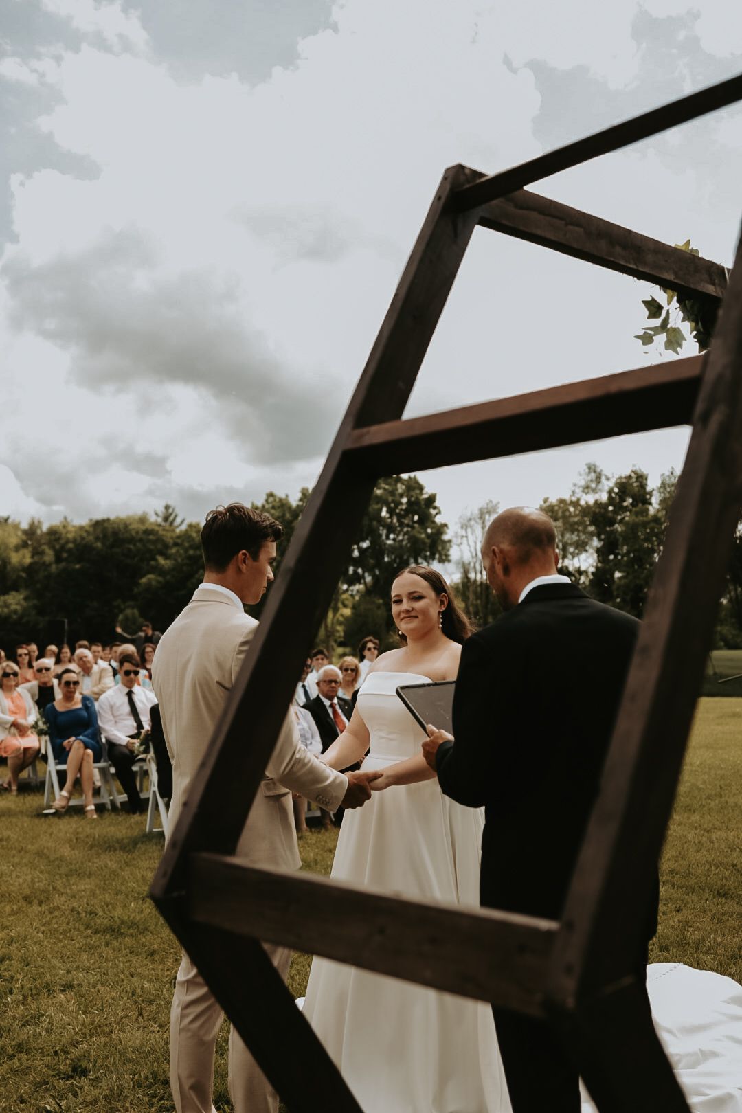 Wedding ceremony captured through geometric wooden frame structure.