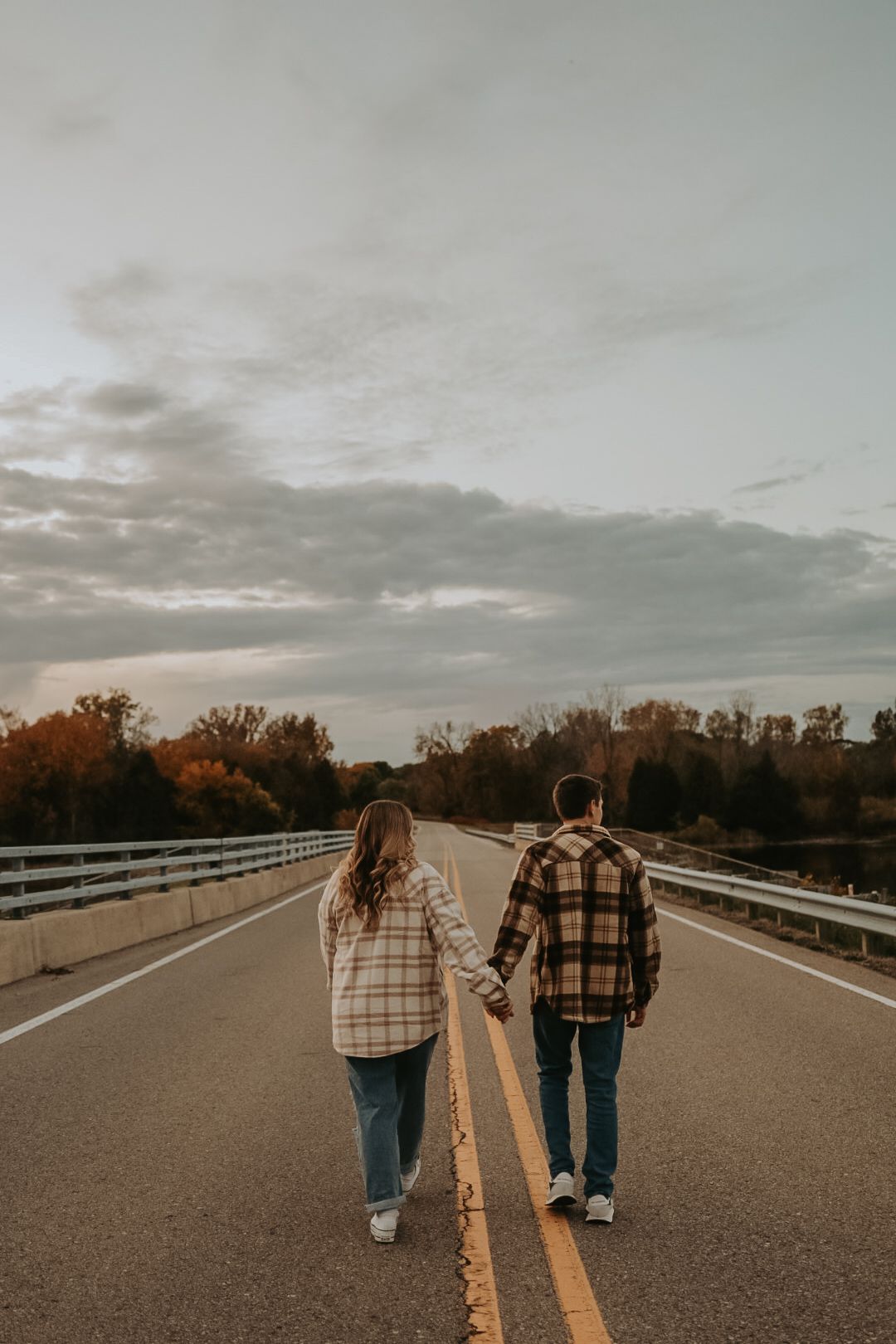 Couple in matching plaid jackets walking hand in hand down empty road at sunset.