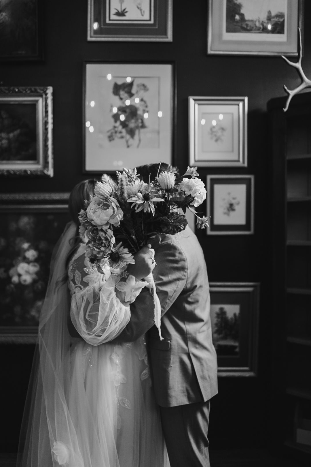 Black and white photo of wedding couple in front of wall with vintage artwork.