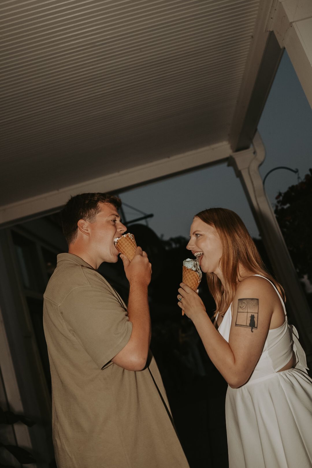 A couple in casual attire playfully interacts in an indoor setting with dramatic lighting.