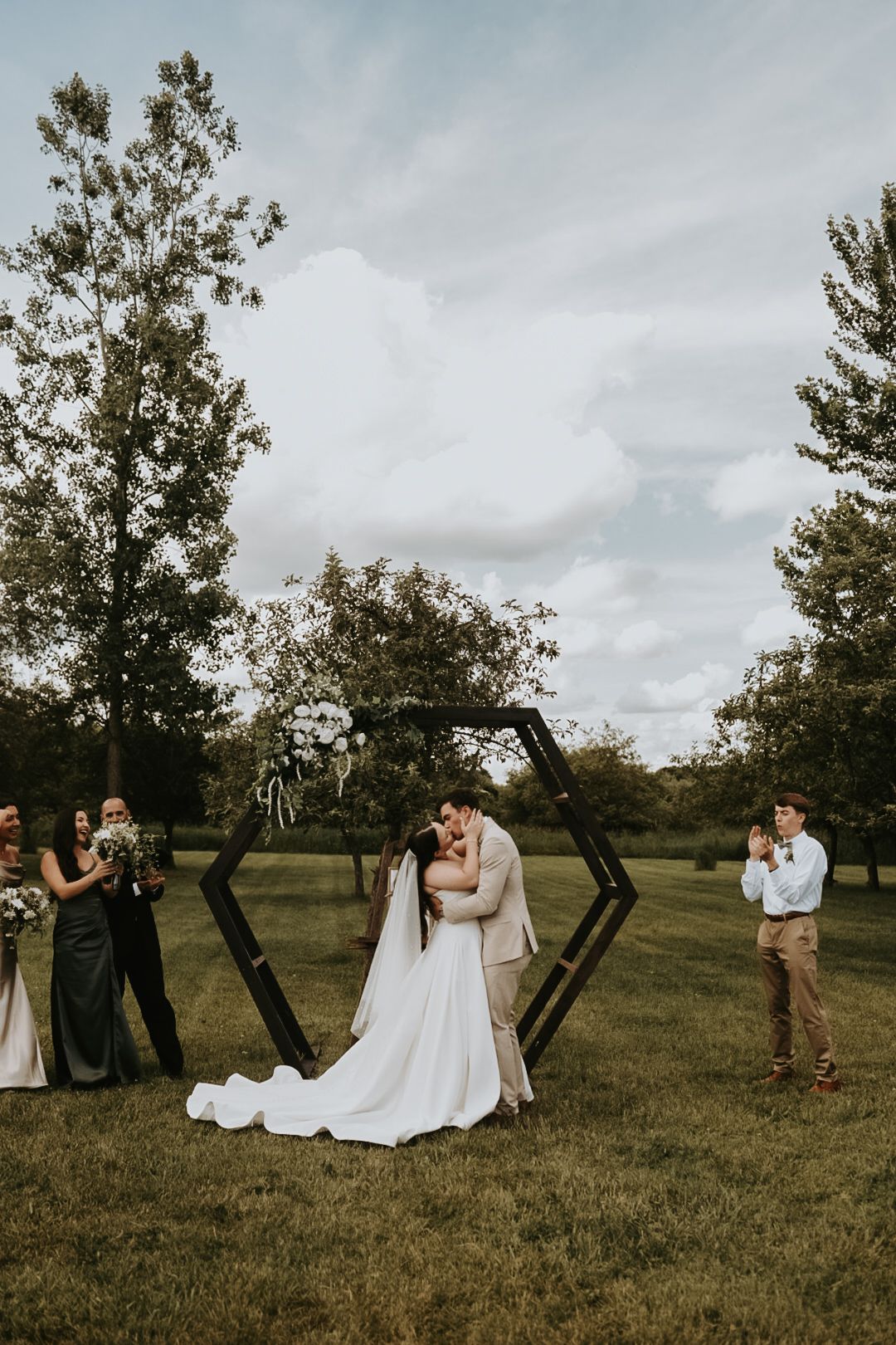 Wedding party poses creatively with wooden geometric frames on grassy field.