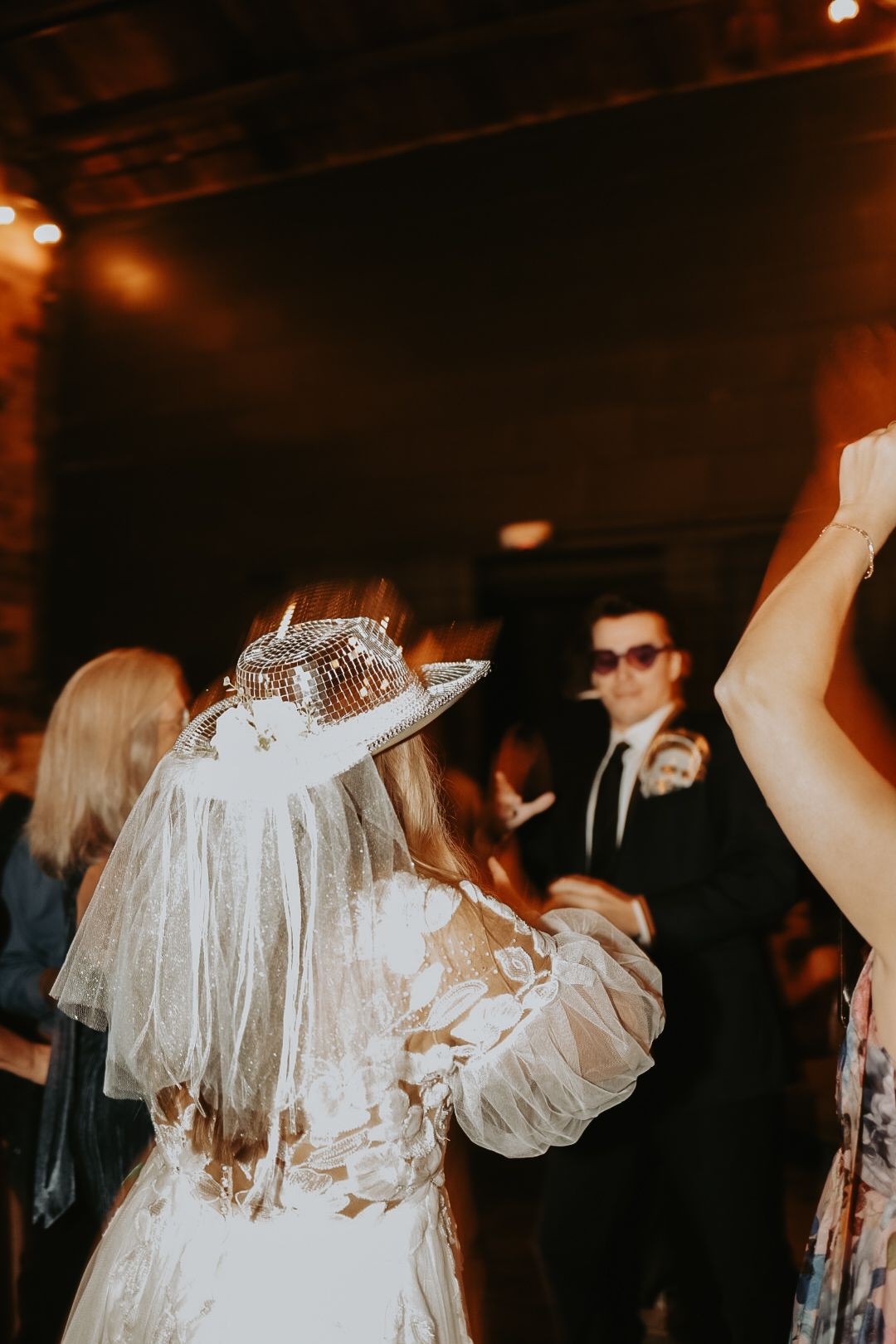 Wedding reception dance party with guests celebrating under warm lighting.