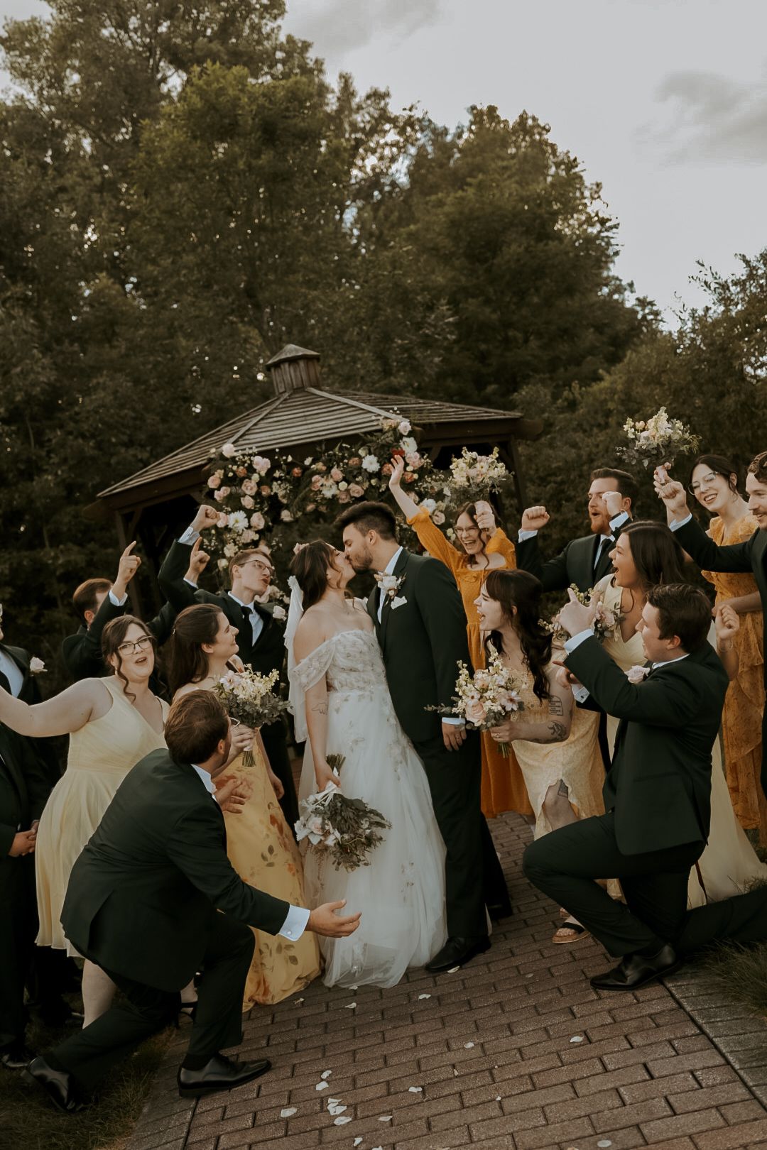 Wedding party celebrates with champagne toast on brick patio during sunset.