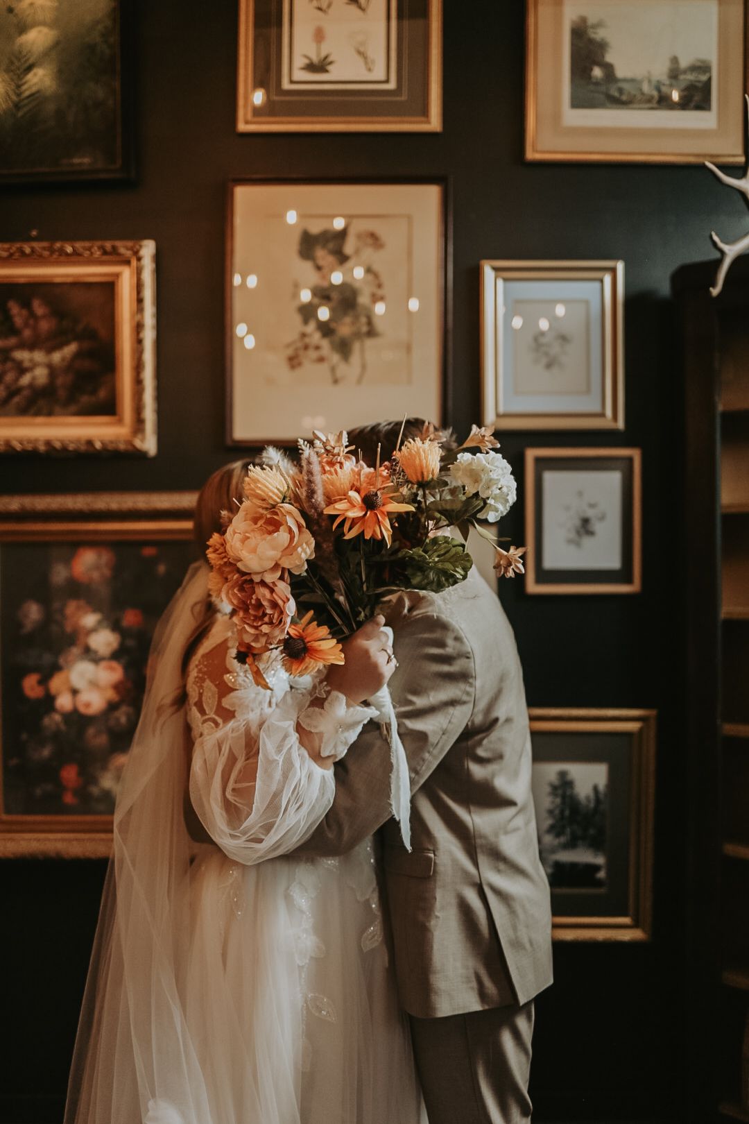 Wedding couple stands in elegant venue with vintage frames and floral arrangements creating romantic ambiance.