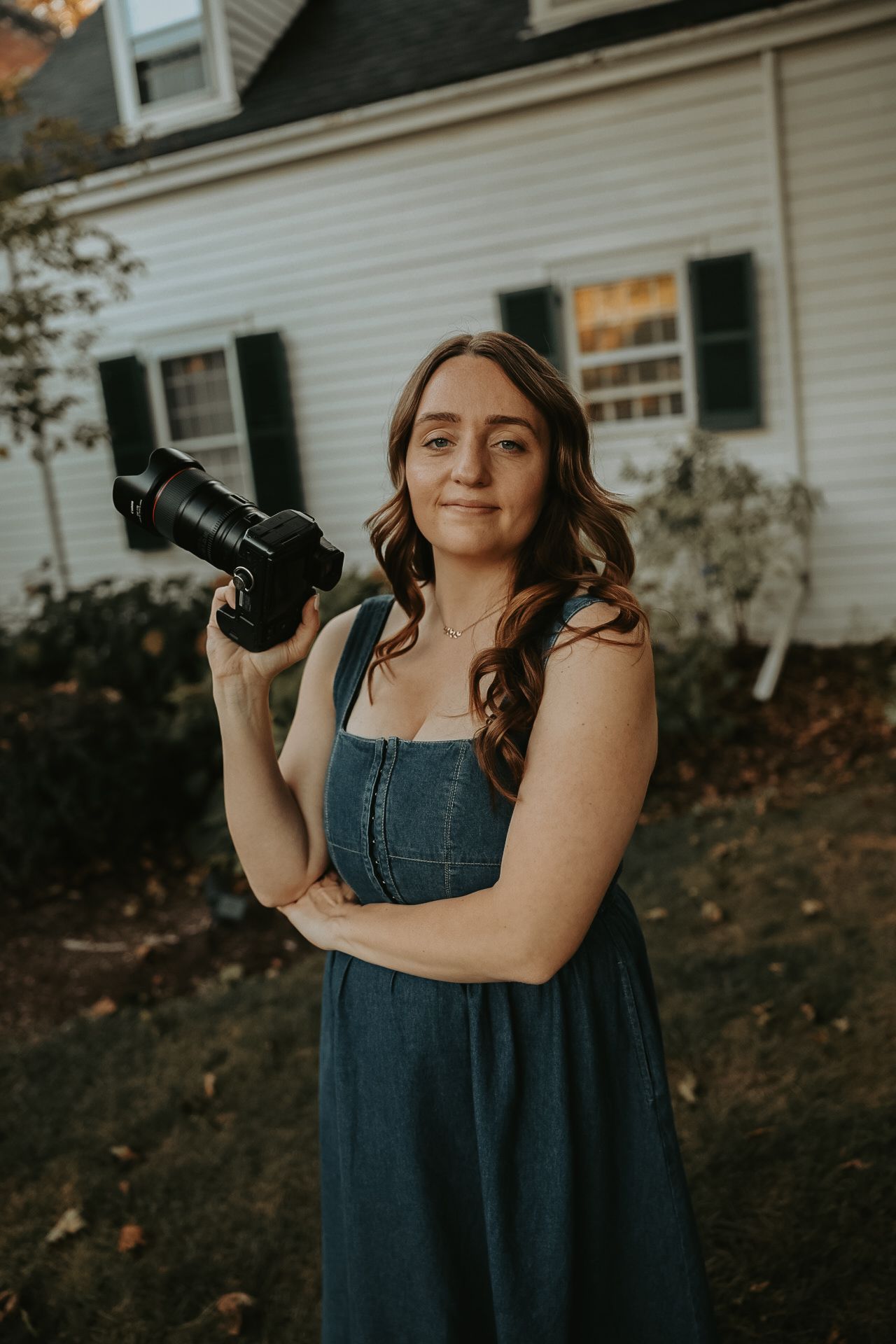 Photographer in denim dress poses with camera equipment outdoors.