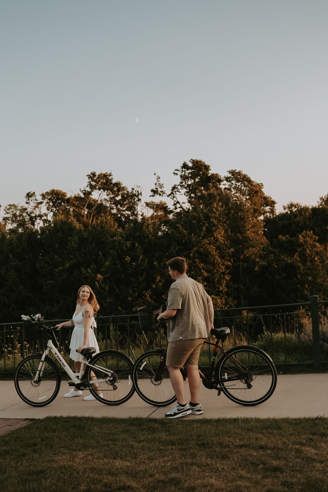 A couple poses playfully with bicycles on a path during golden hour.