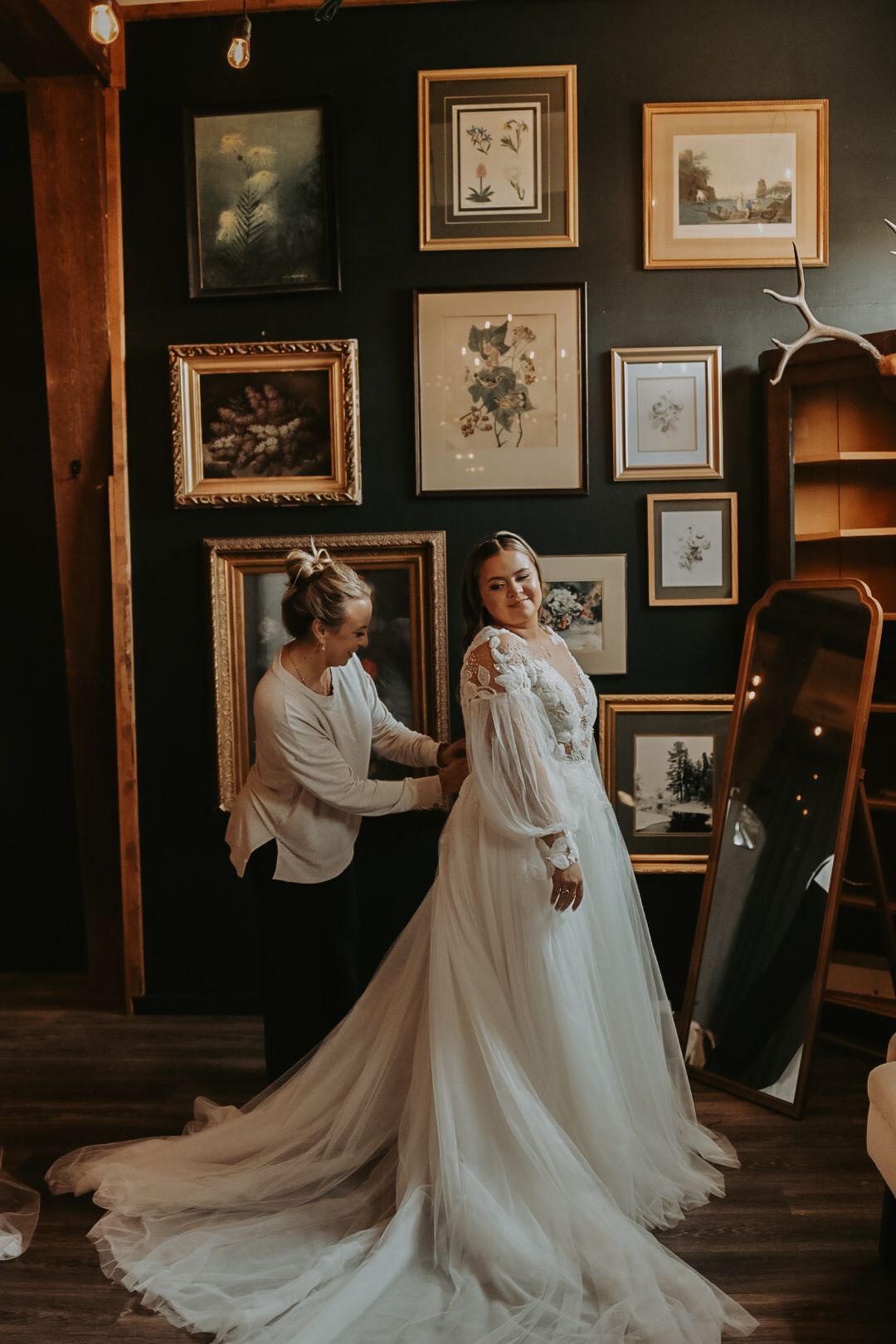 An elegant wedding dress with intricate lace details photographed in a vintage-styled room with gallery walls.