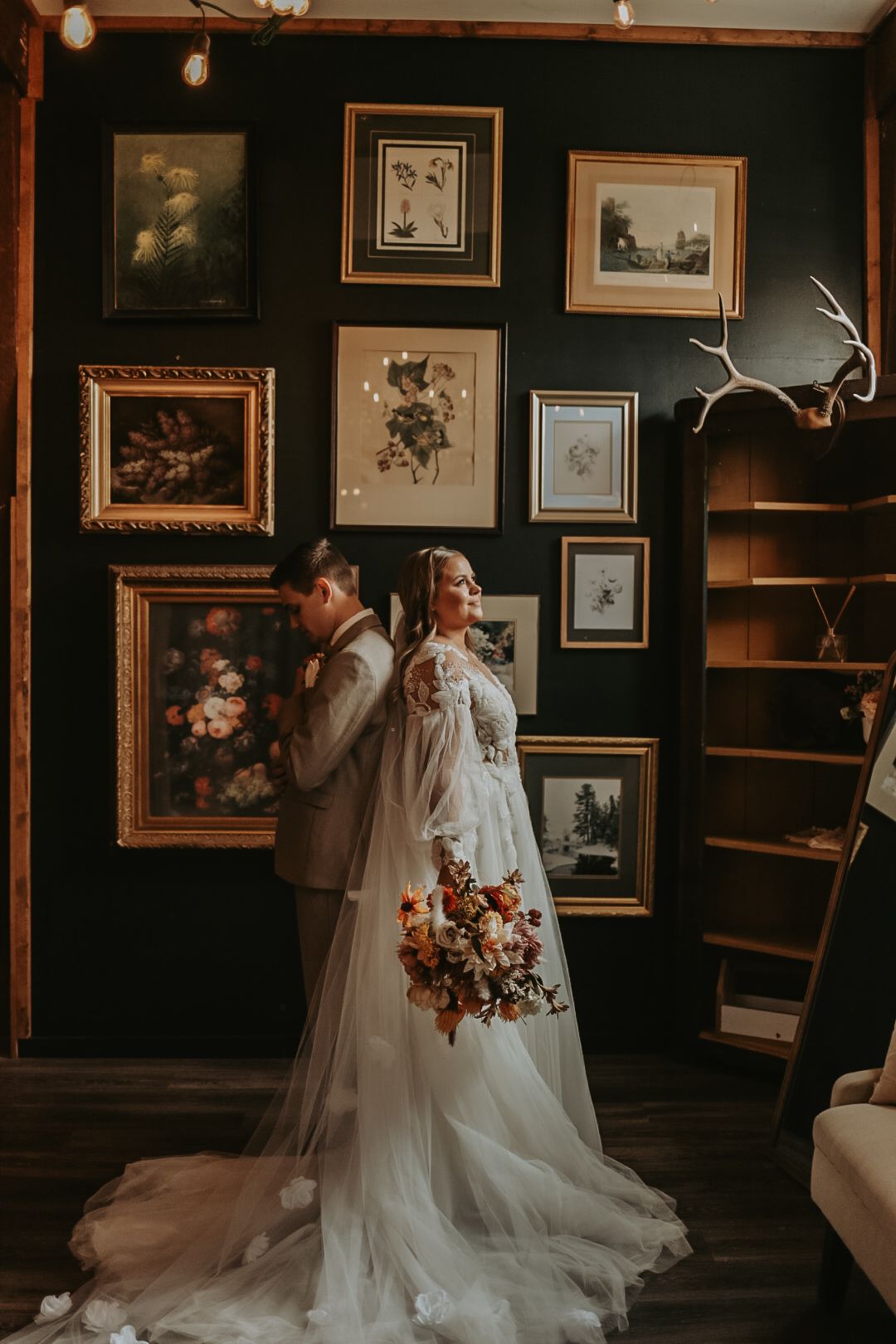 Wedding couple poses in elegant dark room decorated with vintage frames and artwork.